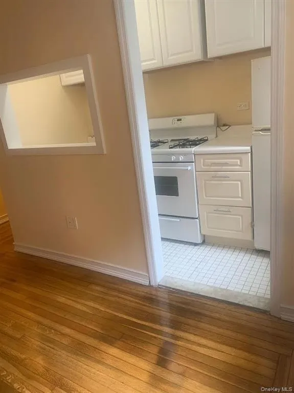 Kitchen featuring white appliances, white cabinets, light wood-style flooring, and light countertops Kitchen featuring white appliances, white cabinets, light wood-style flooring, and light countertops