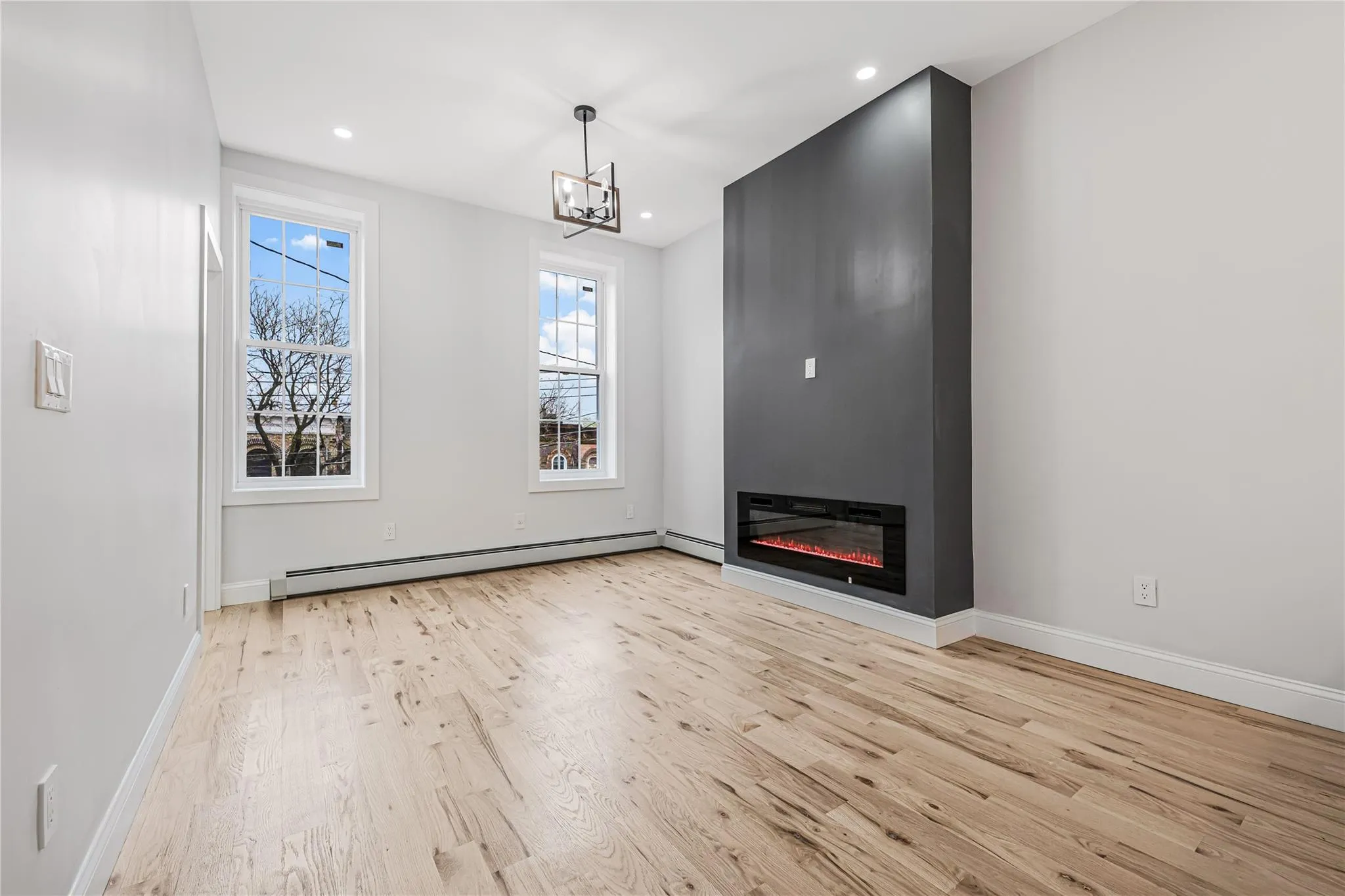Unfurnished living room featuring wood finished floors, a glass covered fireplace, a chandelier, recessed lighting, and a baseboard radiator Unfurnished living room featuring wood finished floors, a glass covered fireplace, a chandelier, recessed lighting, and a baseboard radiator