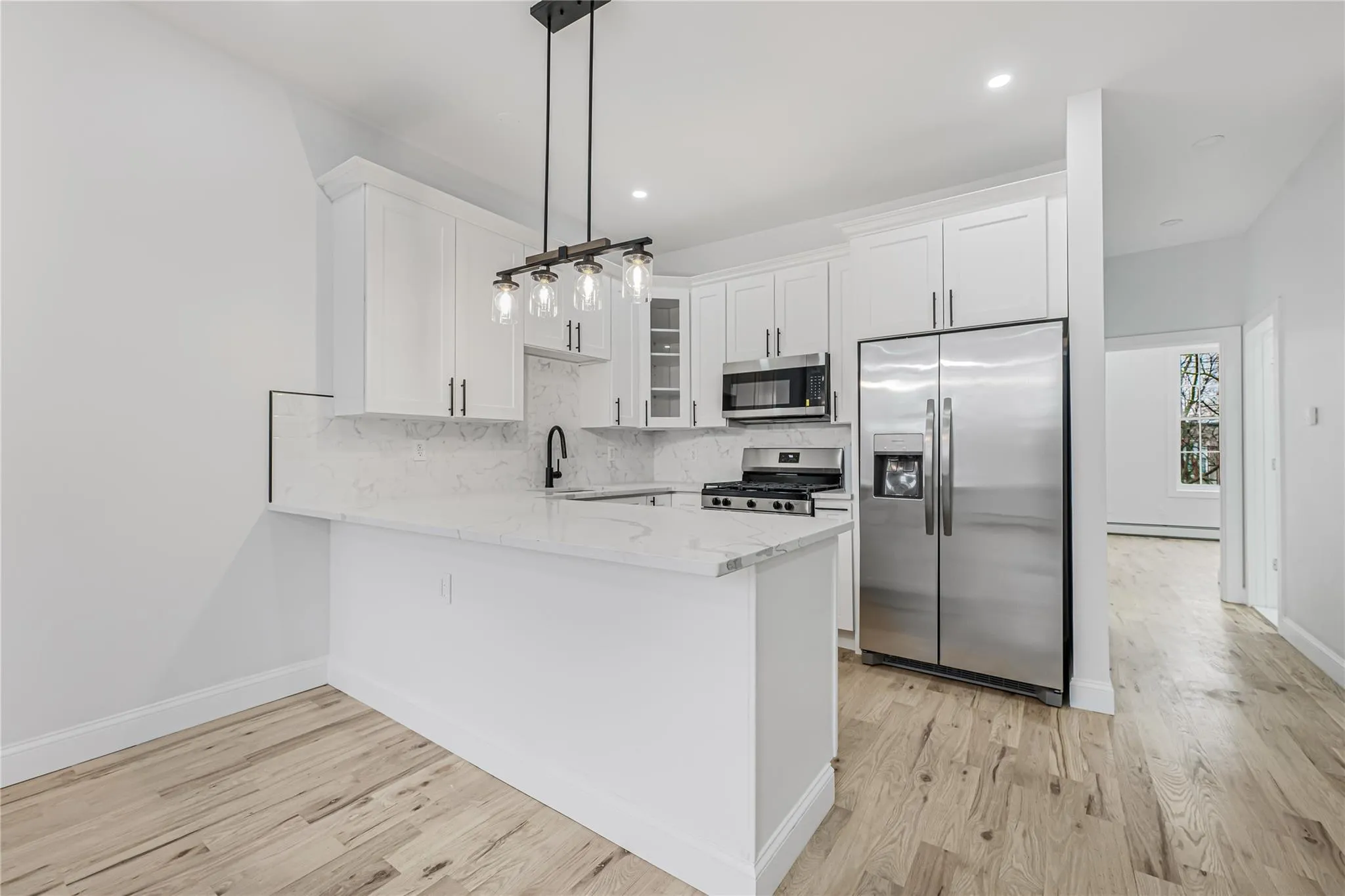 Kitchen featuring appliances with stainless steel finishes, a peninsula, white cabinetry, glass insert cabinets, and light stone countertops Kitchen featuring appliances with stainless steel finishes, a peninsula, white cabinetry, glass insert cabinets, and light stone countertops