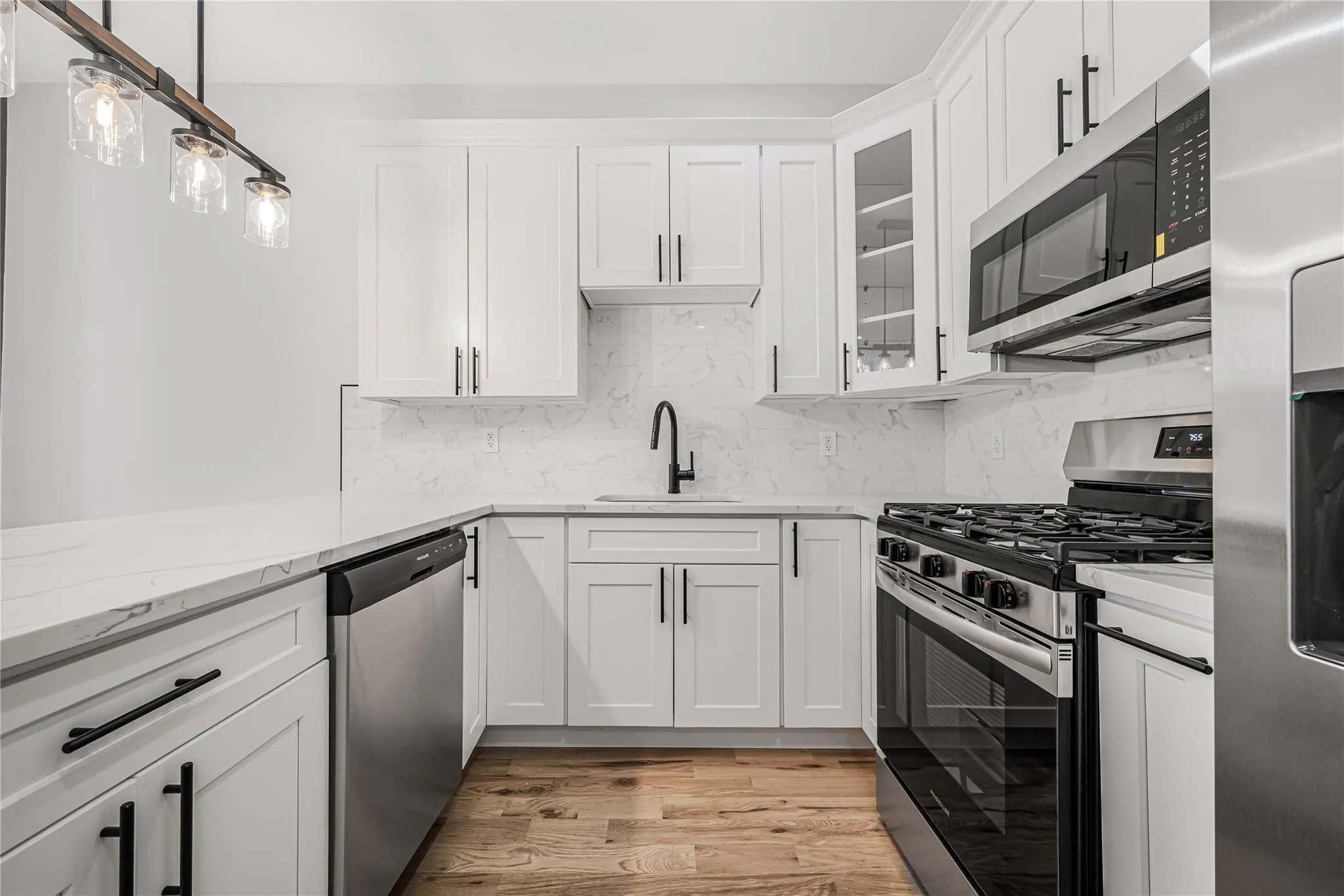 Kitchen with stainless steel appliances, decorative backsplash, white cabinetry, light stone counters, and light wood finished floors Kitchen with stainless steel appliances, decorative backsplash, white cabinetry, light stone counters, and light wood finished floors