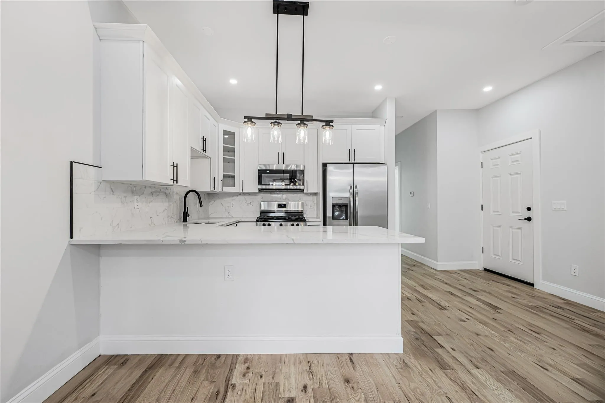 Kitchen with stainless steel appliances, a peninsula, decorative backsplash, light stone counters, and recessed lighting Kitchen with stainless steel appliances, a peninsula, decorative backsplash, light stone counters, and recessed lighting