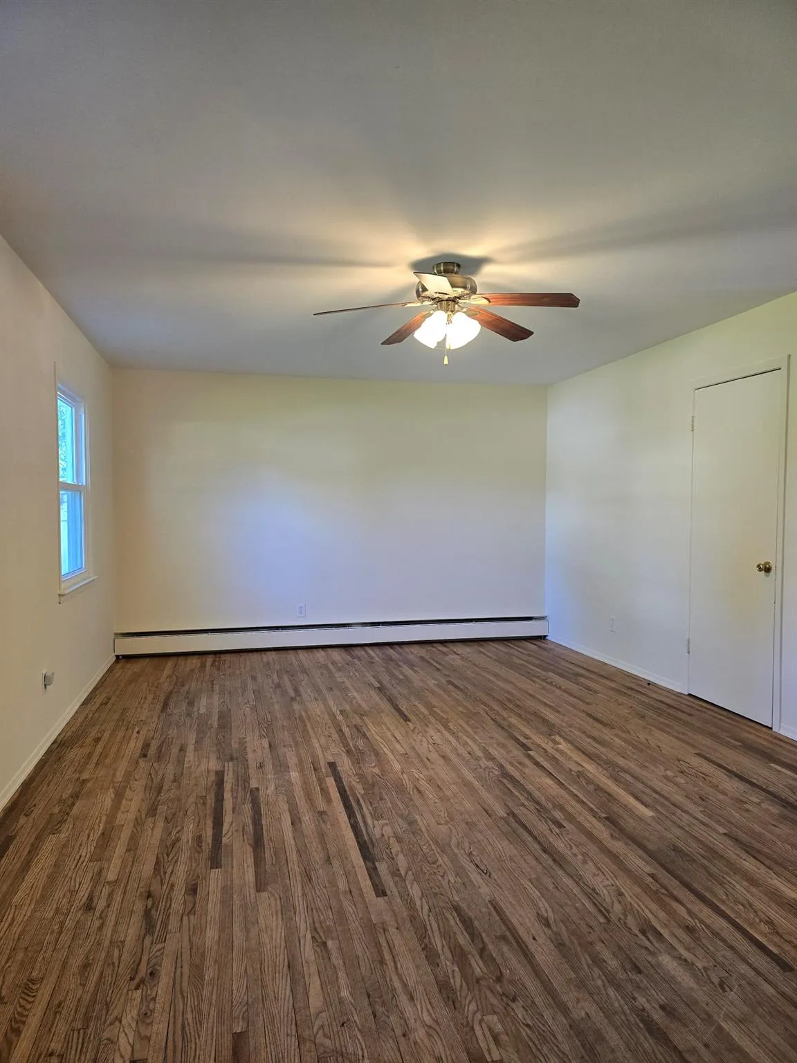 Unfurnished room with dark wood-style flooring, a ceiling fan, and baseboard heating Unfurnished room with dark wood-style flooring, a ceiling fan, and baseboard heating