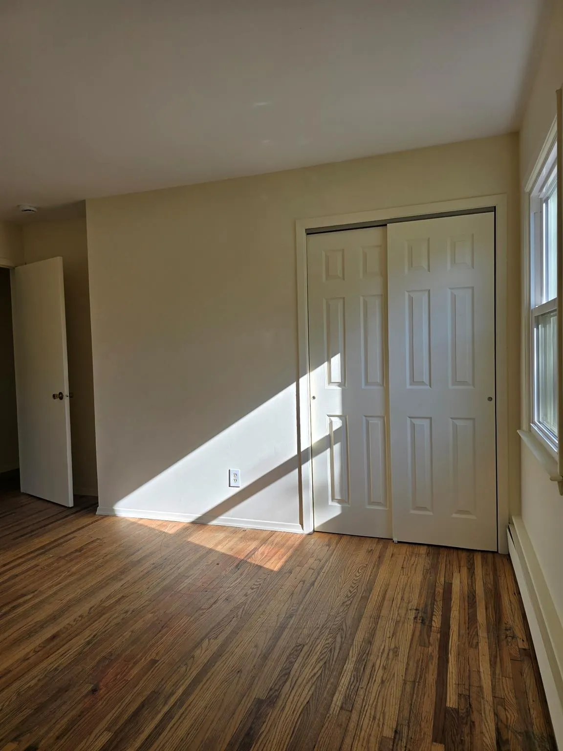 Unfurnished bedroom with dark wood finished floors, a baseboard radiator, and a closet Unfurnished bedroom with dark wood finished floors, a baseboard radiator, and a closet