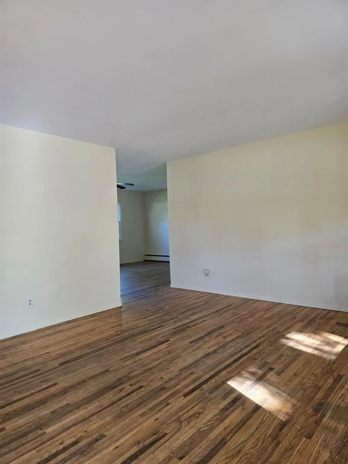 Empty room with dark wood finished floors, ceiling fan, and baseboard heating Empty room with dark wood finished floors, ceiling fan, and baseboard heating