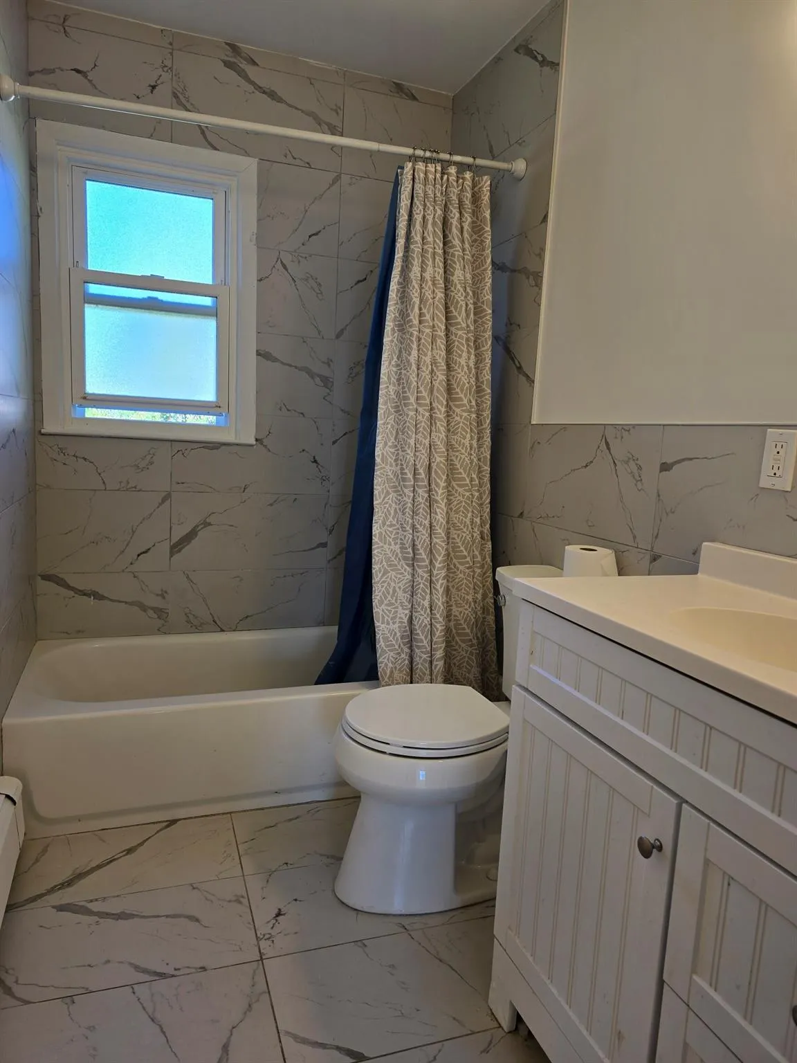 Full bath with marble look tiles, vanity, shower / tub combo with curtain, and tile walls Full bath with marble look tiles, vanity, shower / tub combo with curtain, and tile walls