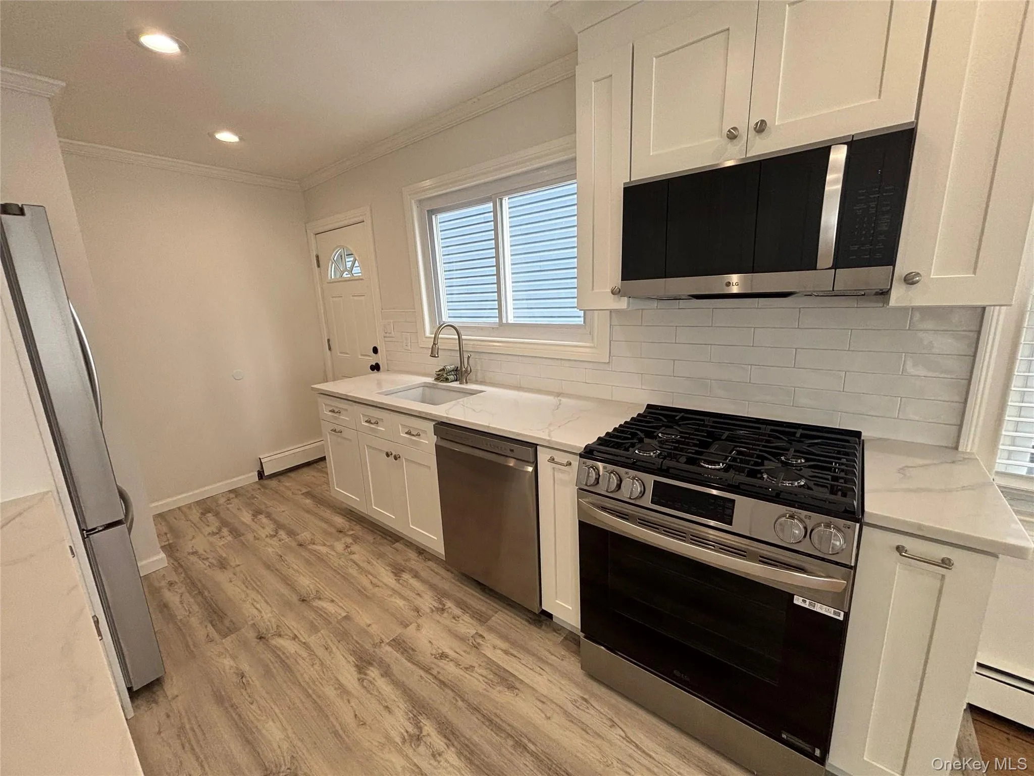 Kitchen featuring appliances with stainless steel finishes, backsplash, white cabinets, crown molding, and light stone counters Kitchen featuring appliances with stainless steel finishes, backsplash, white cabinets, crown molding, and light stone counters