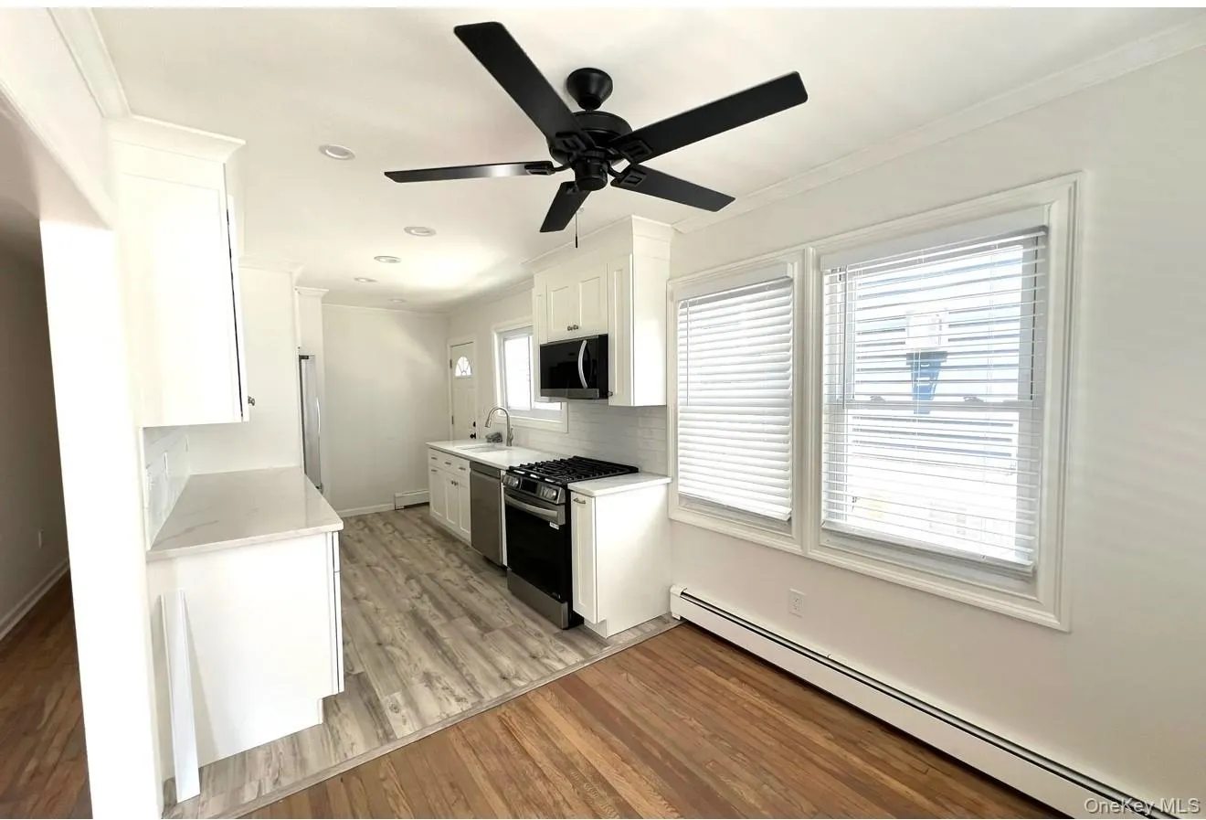 Kitchen with baseboard heating, crown molding, stainless steel appliances, light countertops, and light wood-style flooring Kitchen with baseboard heating, crown molding, stainless steel appliances, light countertops, and light wood-style flooring