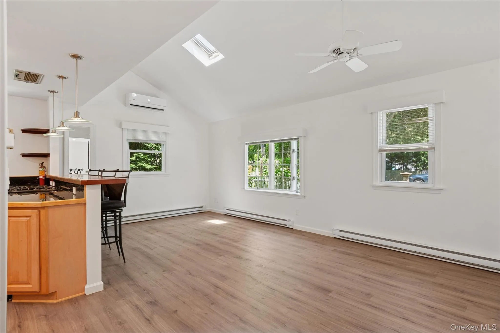 Unfurnished living room with lofted ceiling, light wood-style flooring, baseboard heating, a skylight, and a wall unit AC Unfurnished living room with lofted ceiling, light wood-style flooring, baseboard heating, a skylight, and a wall unit AC