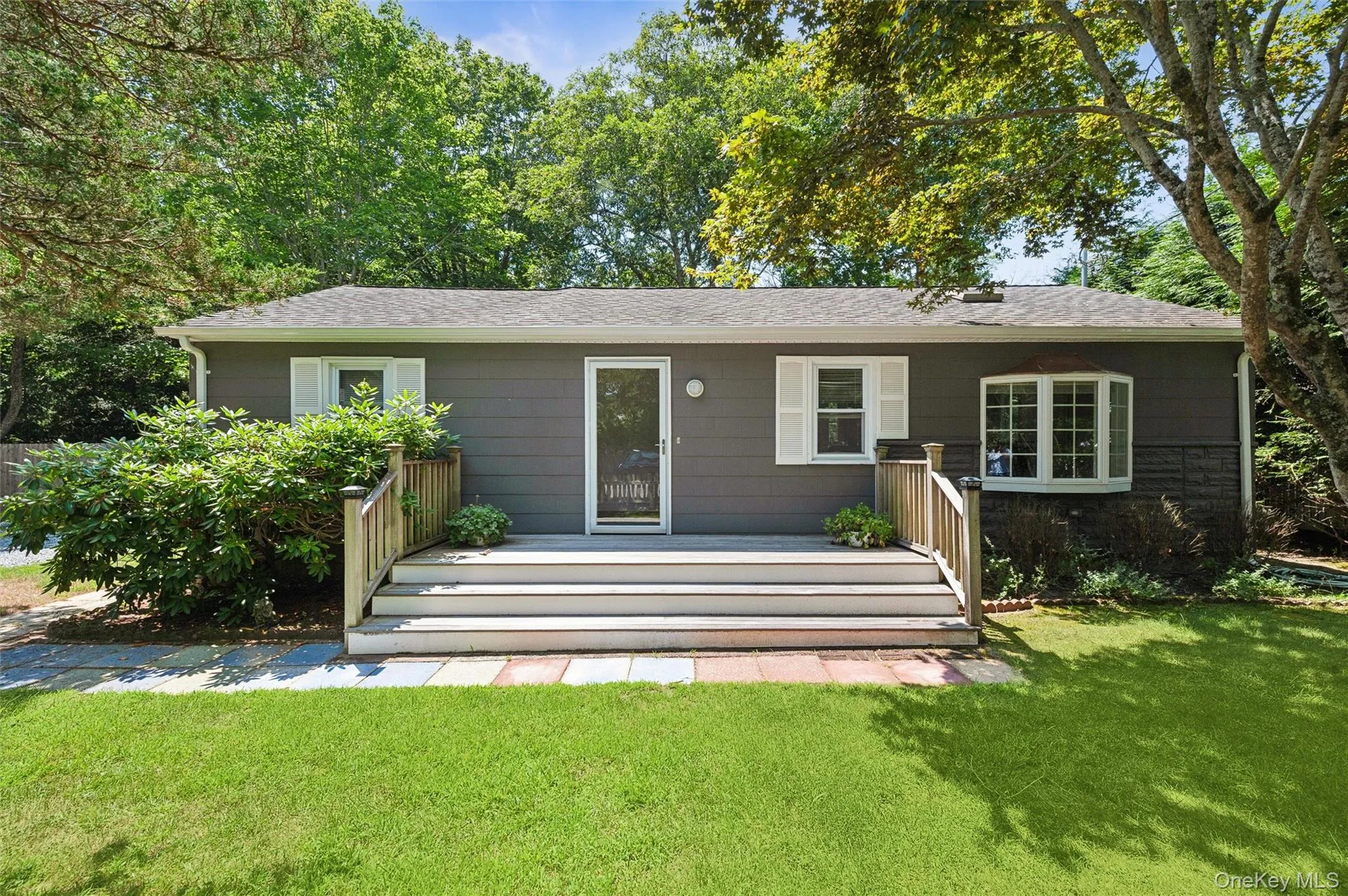 View of front of property with a front yard, a shingled roof, a deck, and stone siding View of front of property with a front yard, a shingled roof, a deck, and stone siding