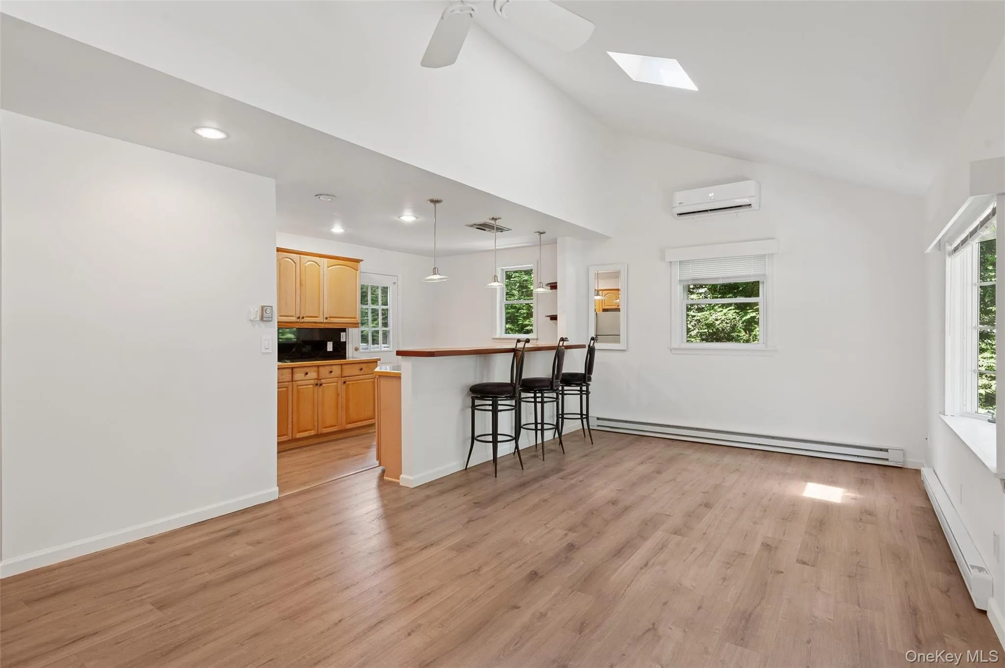 Kitchen featuring a breakfast bar area, light brown cabinets, a baseboard radiator, light wood-style flooring, and vaulted ceiling Kitchen featuring a breakfast bar area, light brown cabinets, a baseboard radiator, light wood-style flooring, and vaulted ceiling