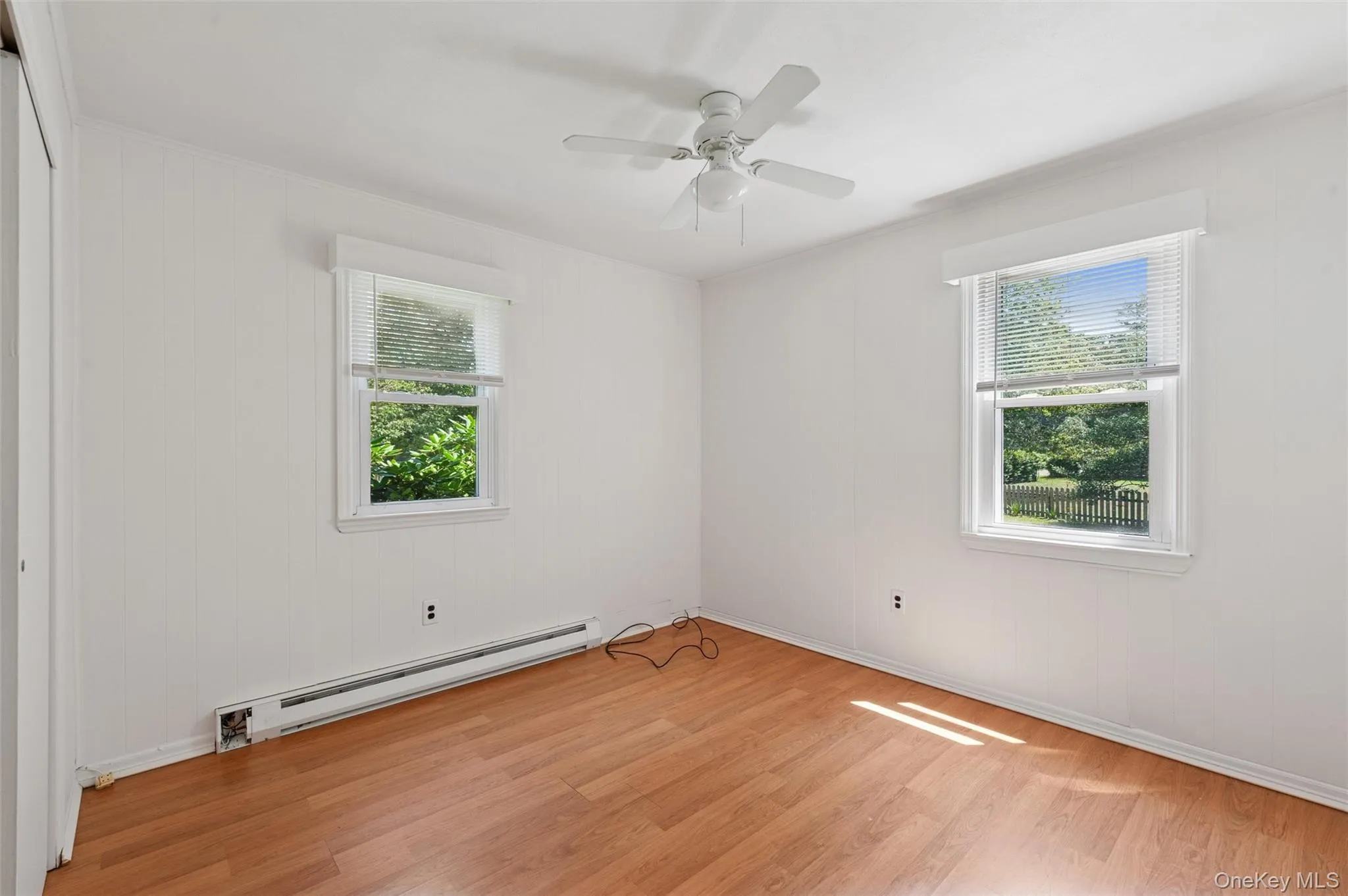 Unfurnished room featuring a baseboard radiator, light wood finished floors, ceiling fan, ornamental molding, and wooden walls Unfurnished room featuring a baseboard radiator, light wood finished floors, ceiling fan, ornamental molding, and wooden walls