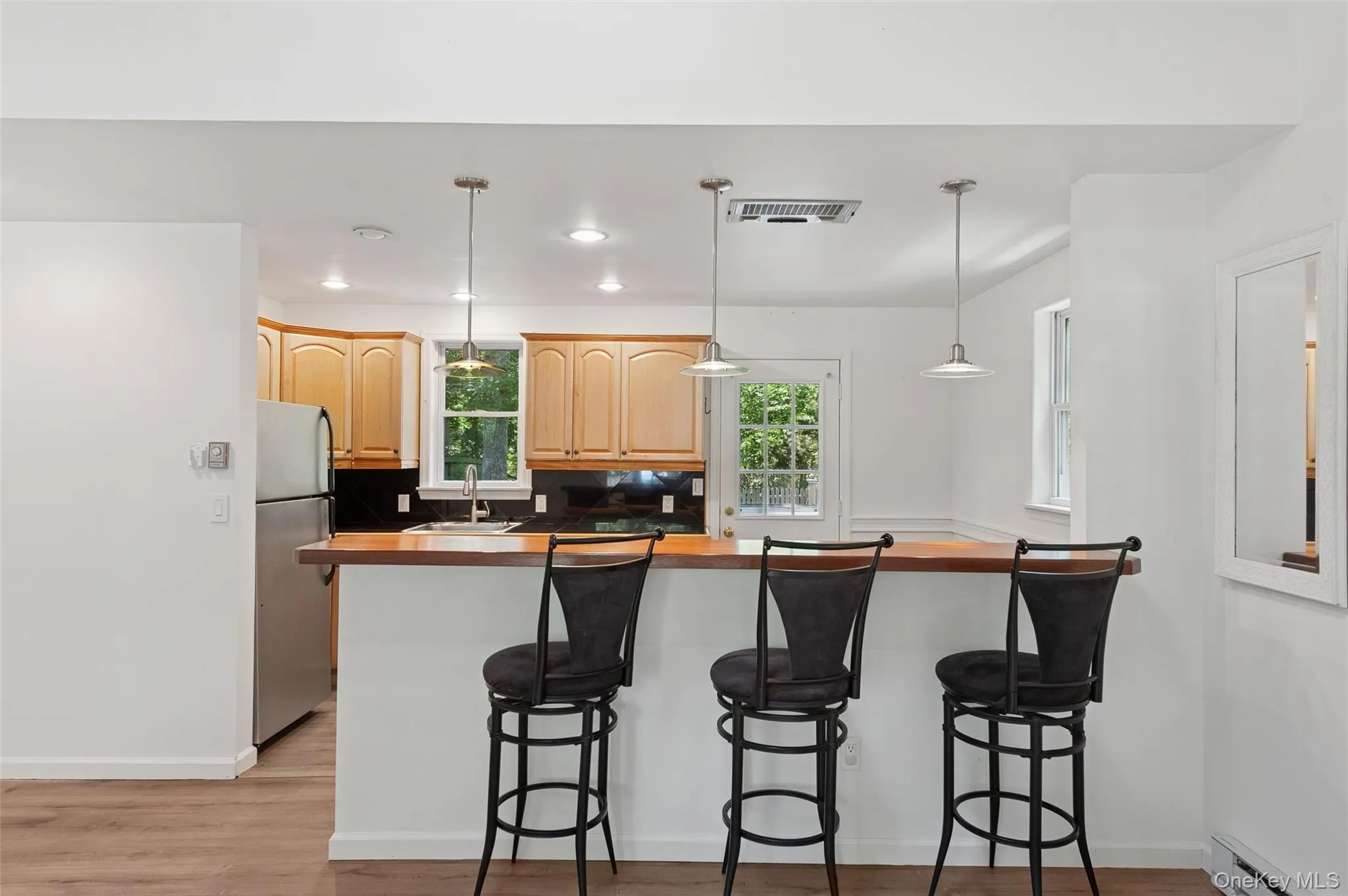 Kitchen with light brown cabinetry, a breakfast bar area, baseboard heating, freestanding refrigerator, and recessed lighting Kitchen with light brown cabinetry, a breakfast bar area, baseboard heating, freestanding refrigerator, and recessed lighting