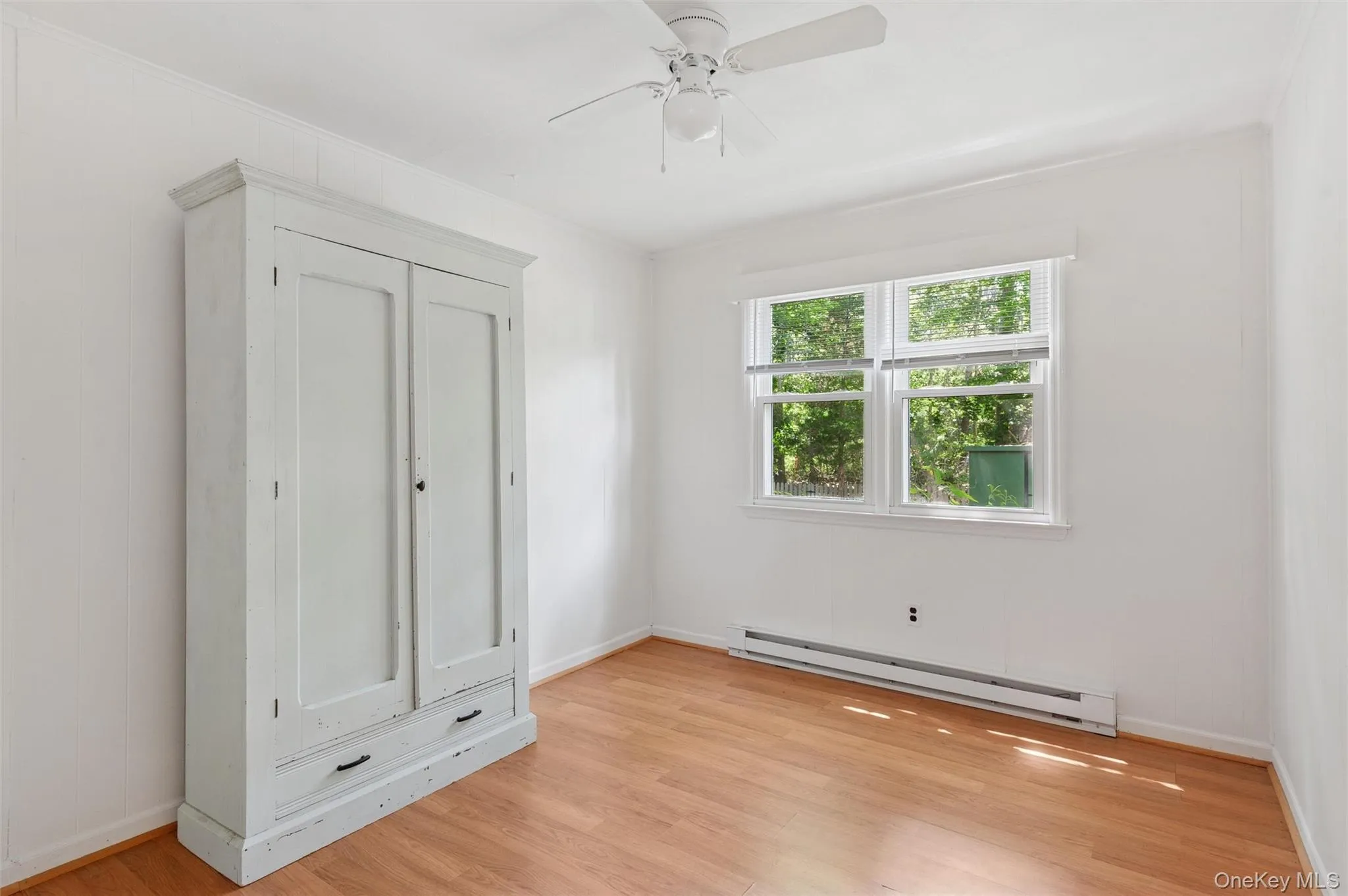 Unfurnished bedroom featuring baseboard heating, ornamental molding, light wood-style floors, and ceiling fan Unfurnished bedroom featuring baseboard heating, ornamental molding, light wood-style floors, and ceiling fan