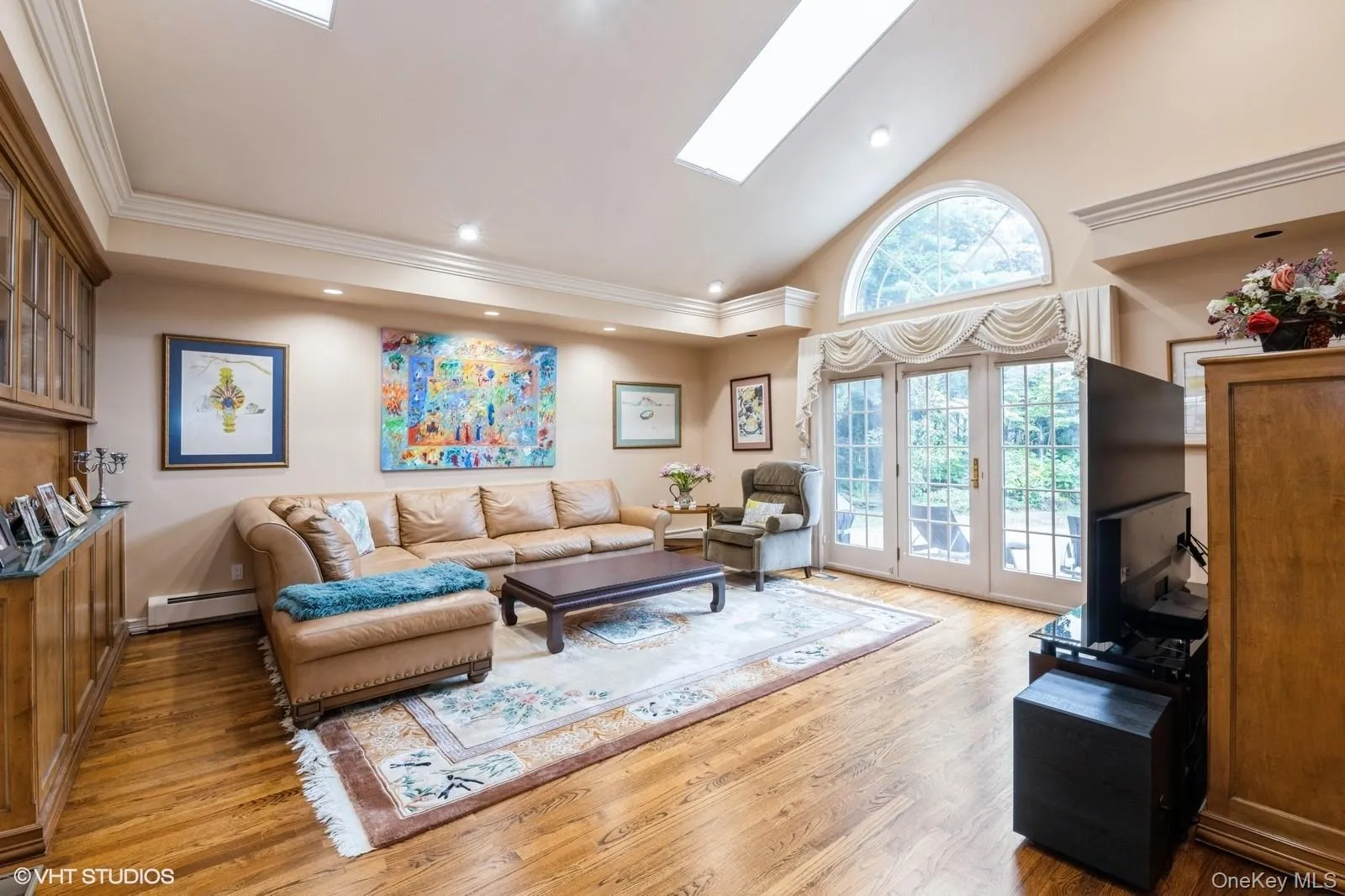 Living room with high vaulted ceiling, a skylight, recessed lighting, light wood-style flooring, and a baseboard radiator Living room with high vaulted ceiling, a skylight, recessed lighting, light wood-style flooring, and a baseboard radiator