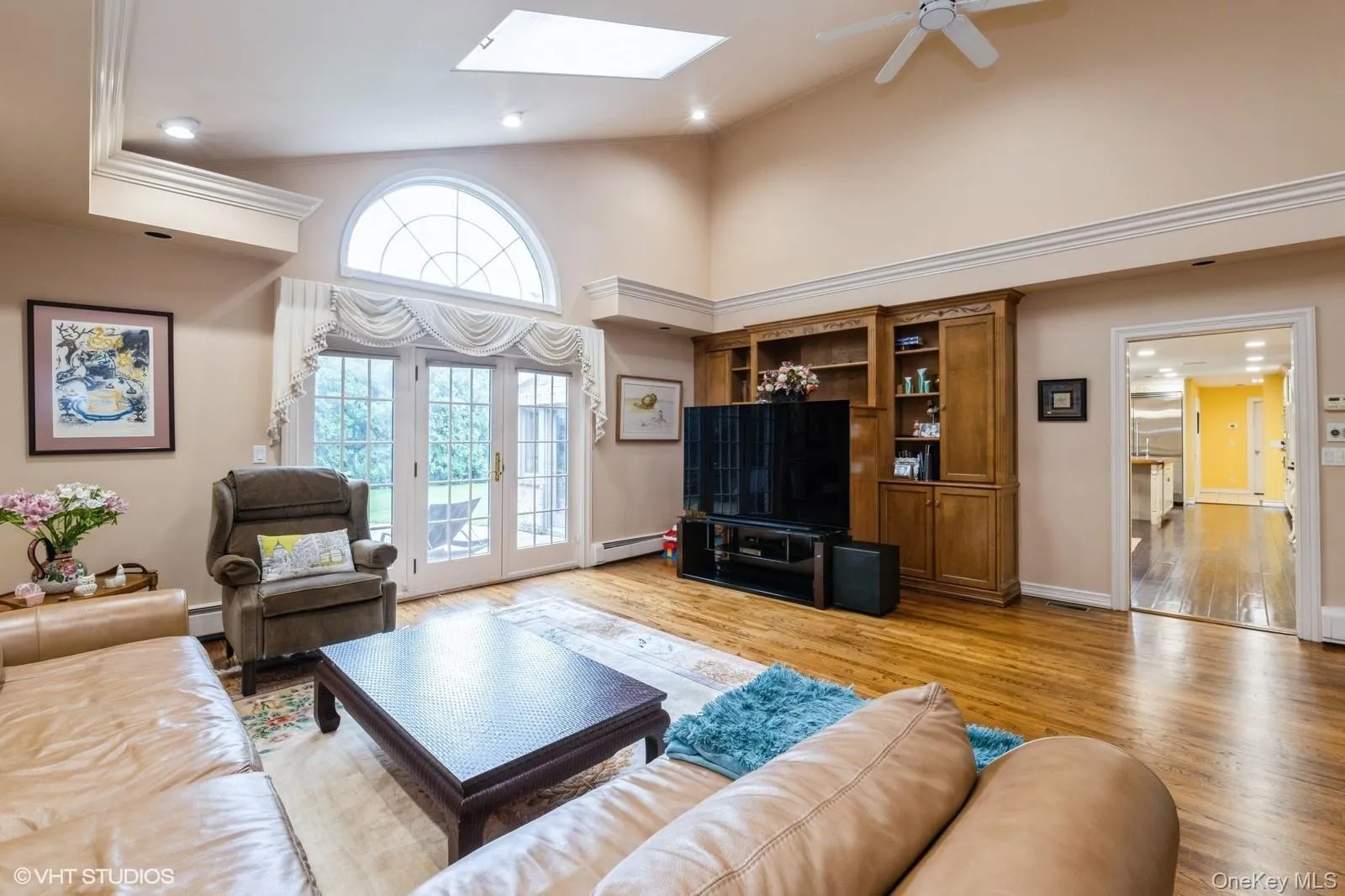 Living room featuring high vaulted ceiling, light wood finished floors, a skylight, a baseboard heating unit, and a ceiling fan Living room featuring high vaulted ceiling, light wood finished floors, a skylight, a baseboard heating unit, and a ceiling fan