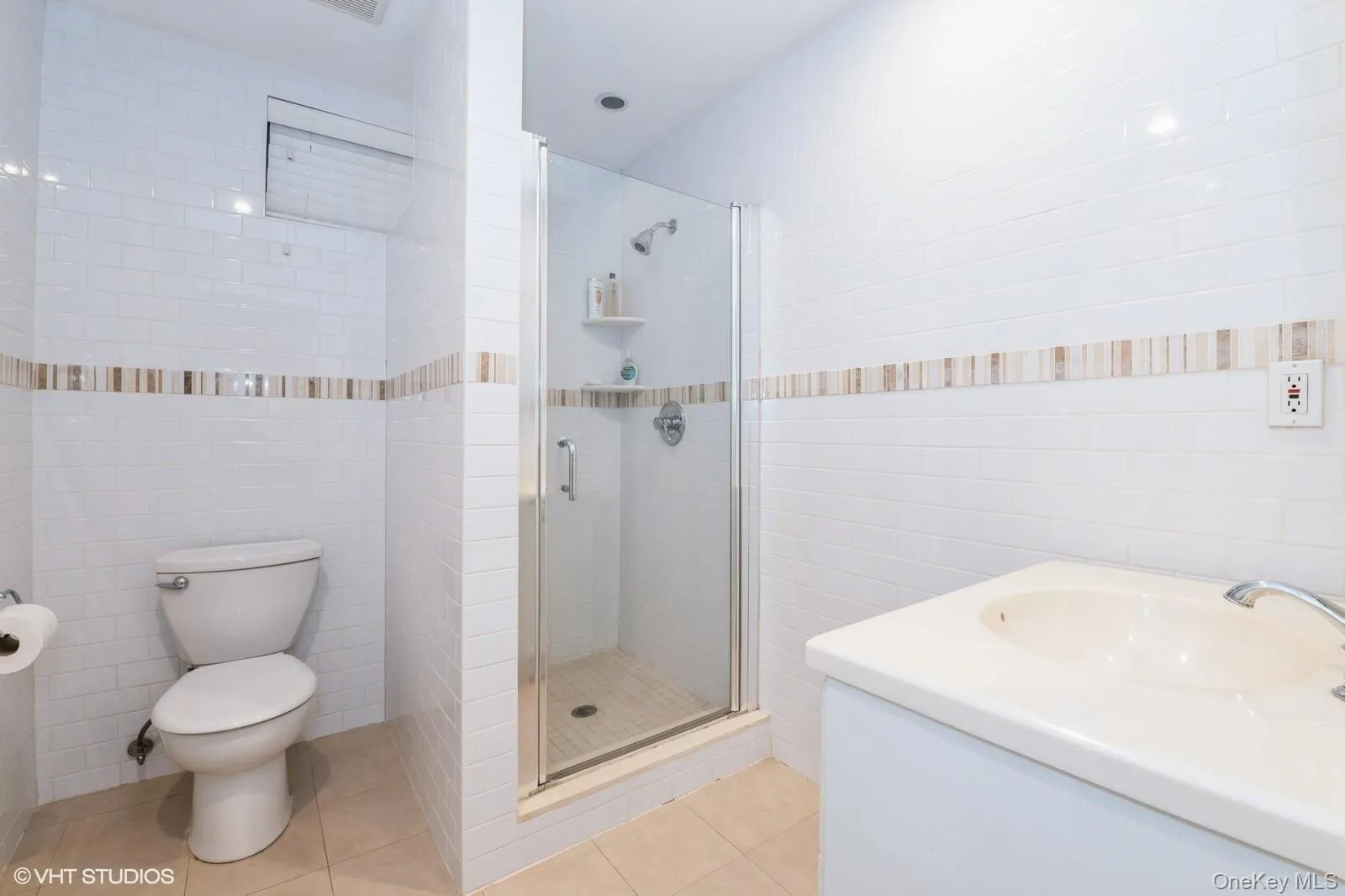 Bathroom with tile walls, a shower stall, vanity, and light tile patterned floors Bathroom with tile walls, a shower stall, vanity, and light tile patterned floors
