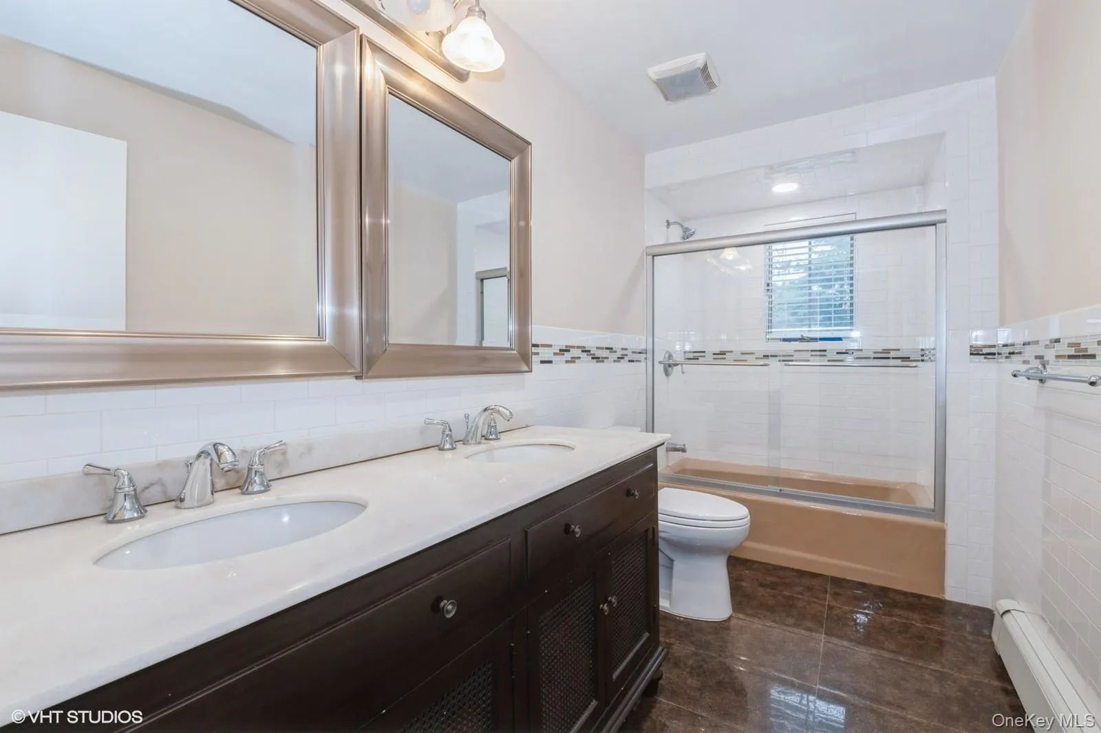 Bathroom featuring bath / shower combo with glass door, tile walls, a baseboard heating unit, and dark tile patterned floors Bathroom featuring bath / shower combo with glass door, tile walls, a baseboard heating unit, and dark tile patterned floors