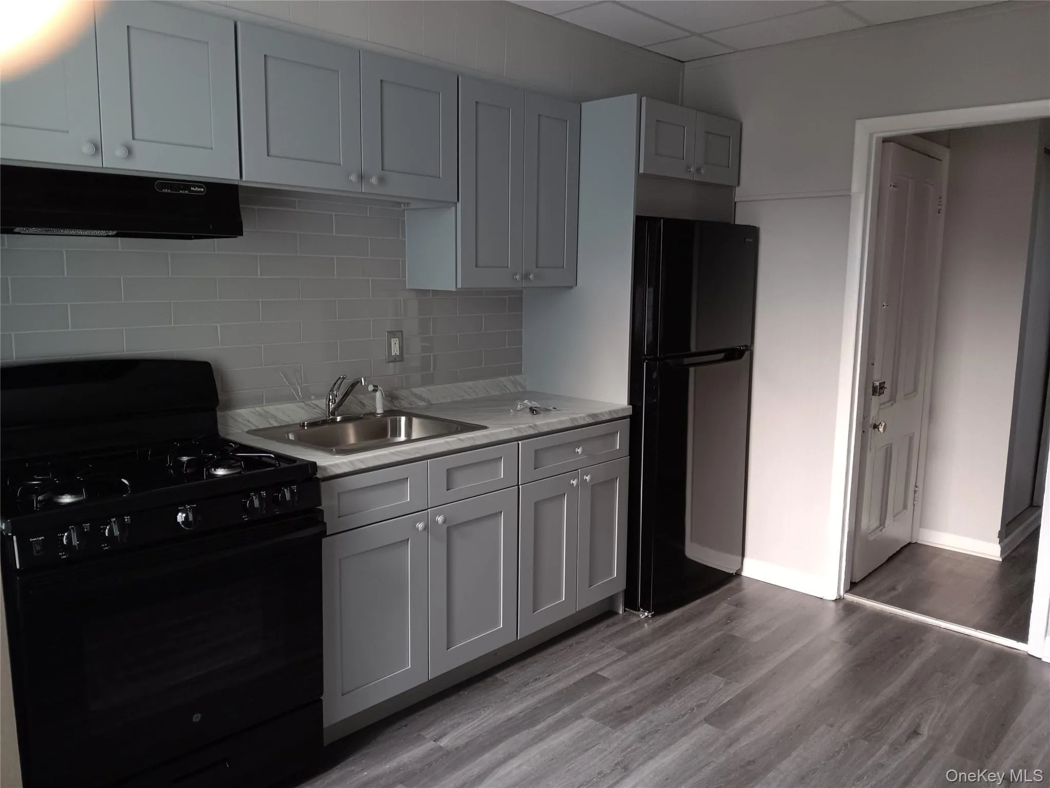 Kitchen with black appliances, range hood, light countertops, backsplash, and light wood-style floors Kitchen with black appliances, range hood, light countertops, backsplash, and light wood-style floors