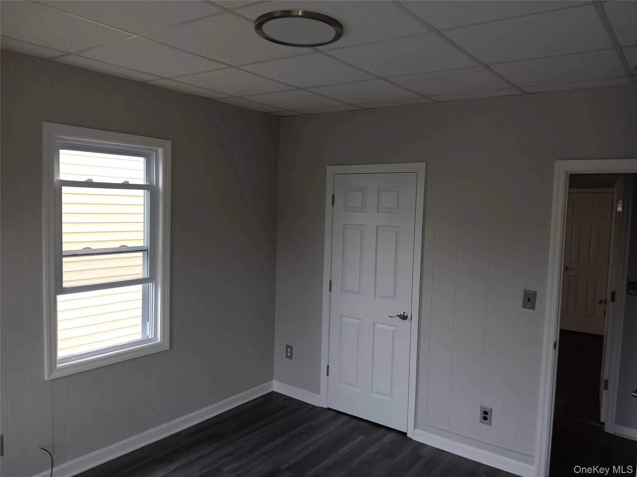 Unfurnished bedroom with a paneled ceiling, dark wood-style floors, and wood walls Unfurnished bedroom with a paneled ceiling, dark wood-style floors, and wood walls