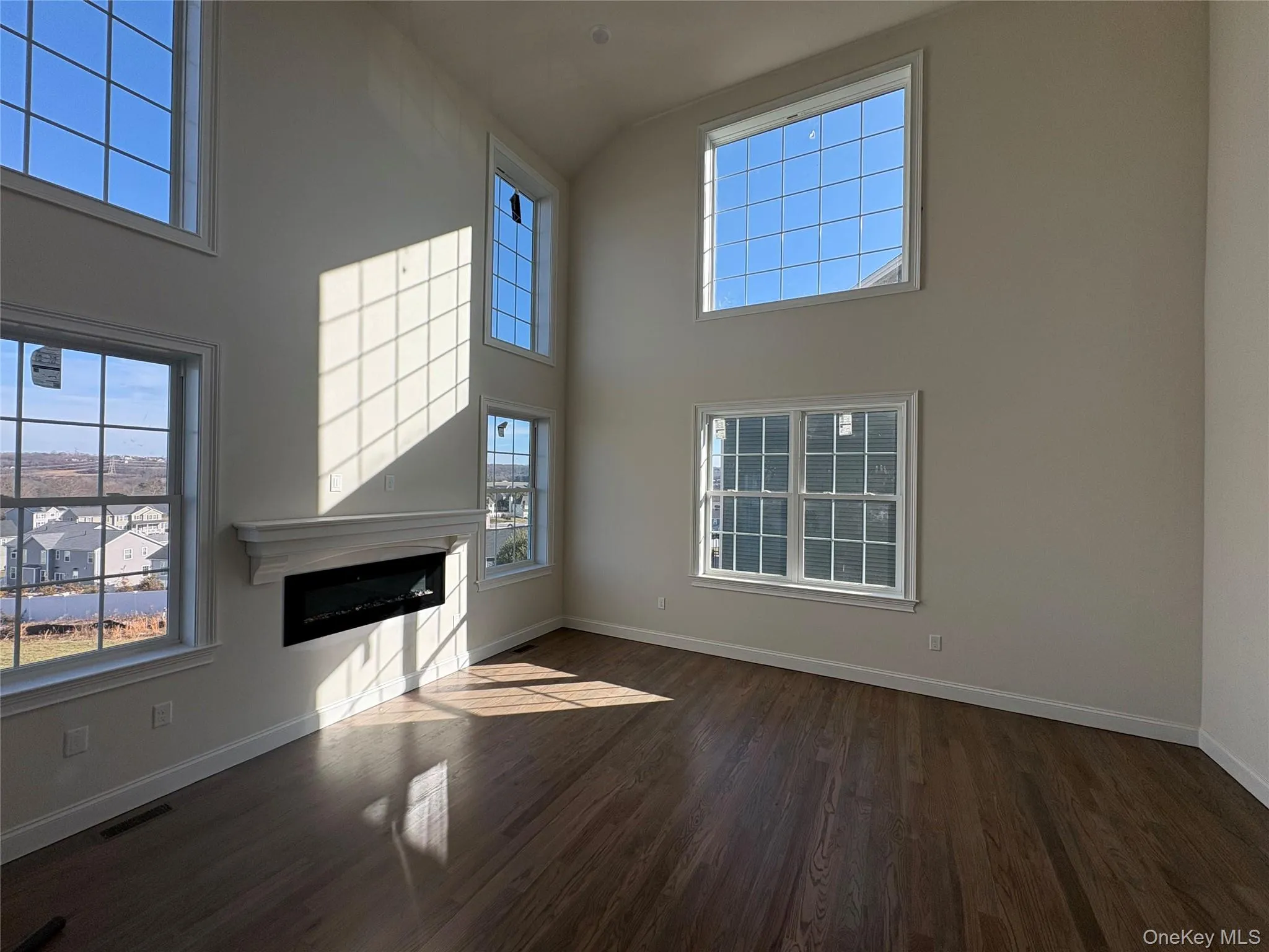 Unfurnished living room with a glass covered fireplace, dark wood-type flooring, and a high ceiling Unfurnished living room with a glass covered fireplace, dark wood-type flooring, and a high ceiling