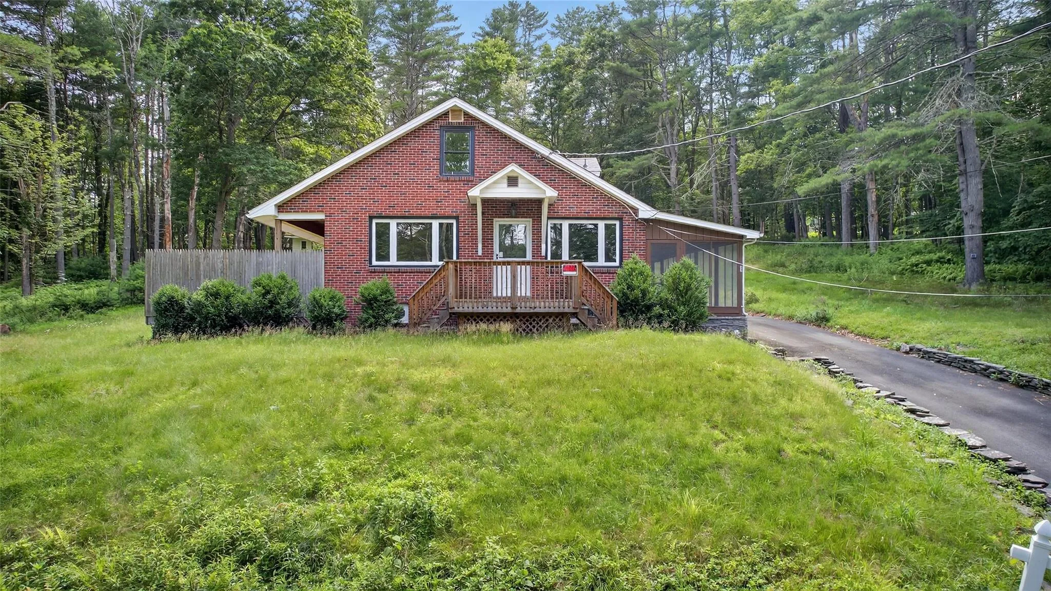 View of front facade featuring asphalt driveway, brick siding, a front lawn, and a wooded view View of front facade featuring asphalt driveway, brick siding, a front lawn, and a wooded view