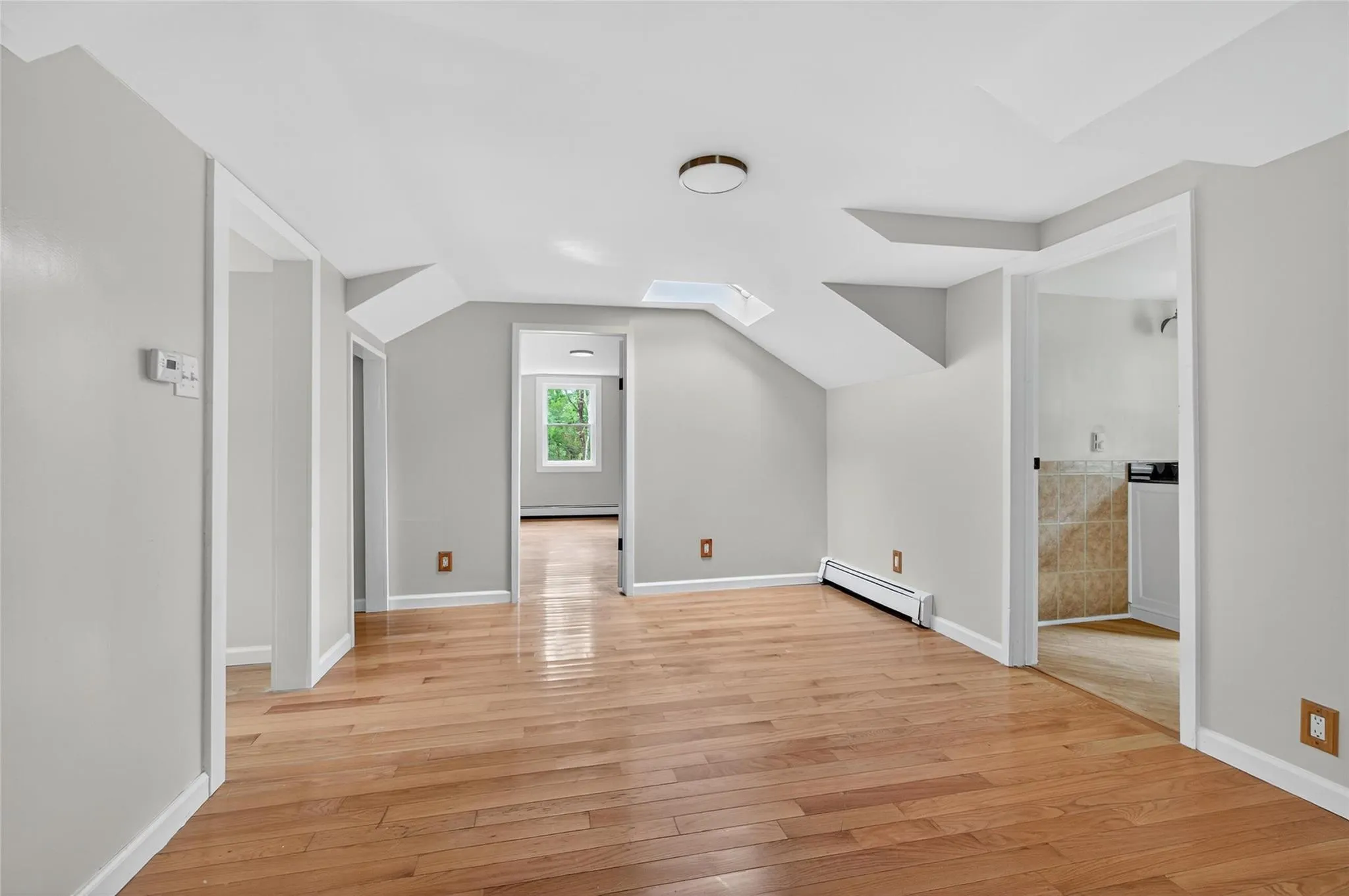 Additional living space featuring a baseboard heating unit, light wood-style floors, a skylight, and lofted ceiling Additional living space featuring a baseboard heating unit, light wood-style floors, a skylight, and lofted ceiling