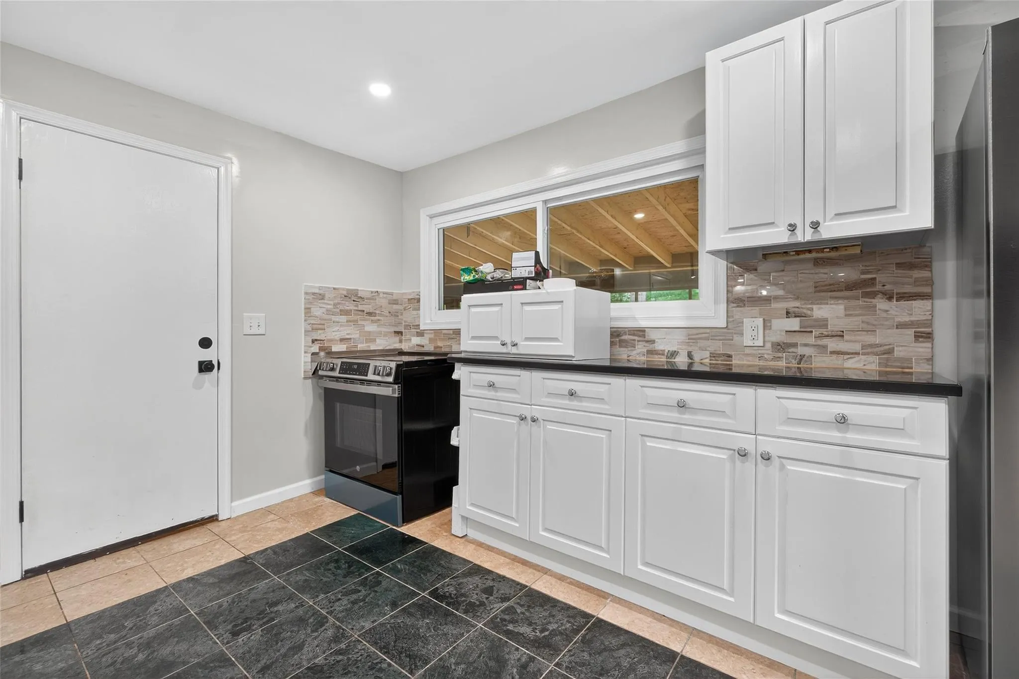 Kitchen with stainless steel range with electric stovetop, backsplash, dark countertops, white cabinetry, and recessed lighting Kitchen with stainless steel range with electric stovetop, backsplash, dark countertops, white cabinetry, and recessed lighting