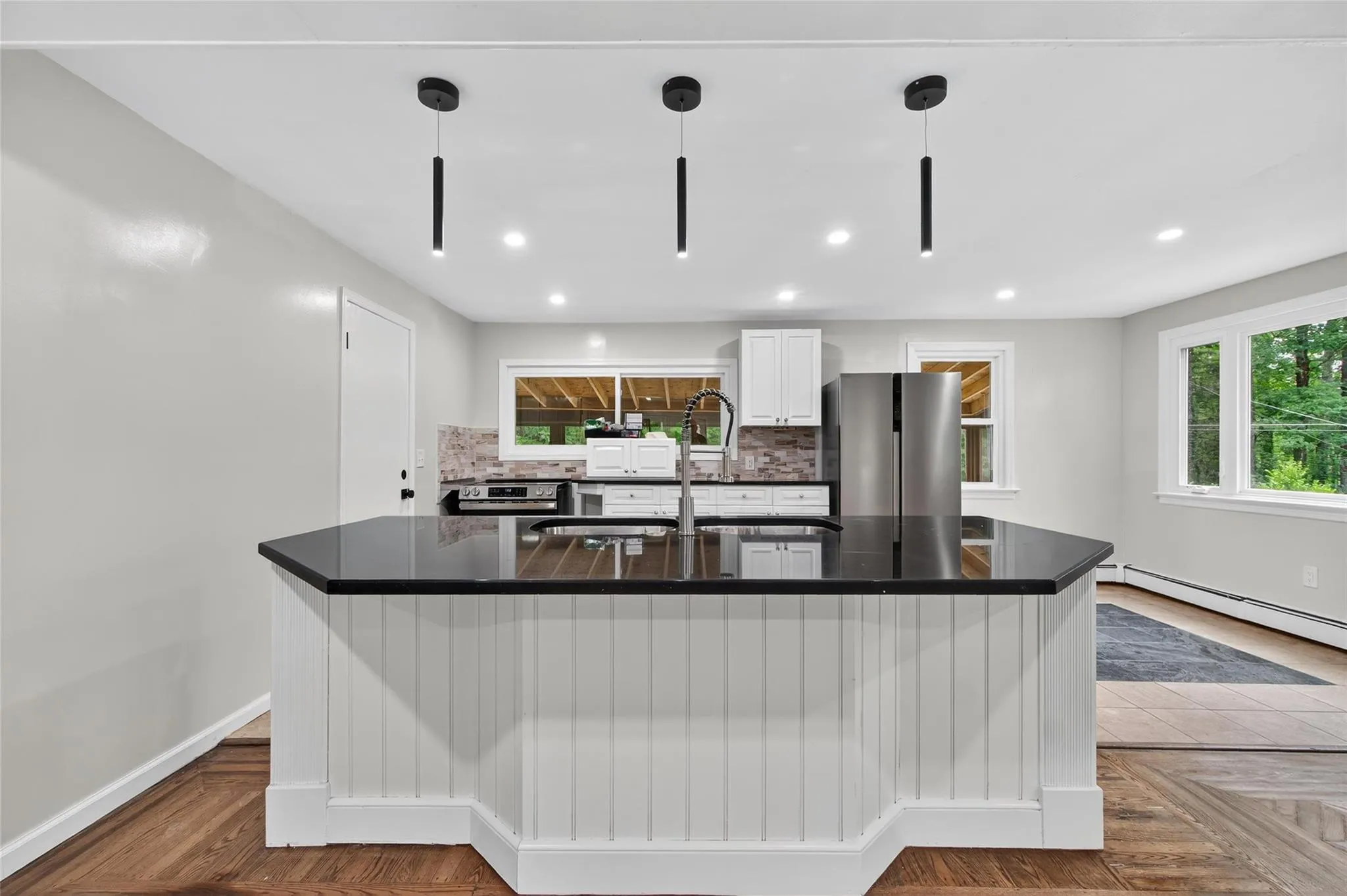 Kitchen with freestanding refrigerator, dark countertops, tasteful backsplash, a baseboard radiator, and a large island Kitchen with freestanding refrigerator, dark countertops, tasteful backsplash, a baseboard radiator, and a large island