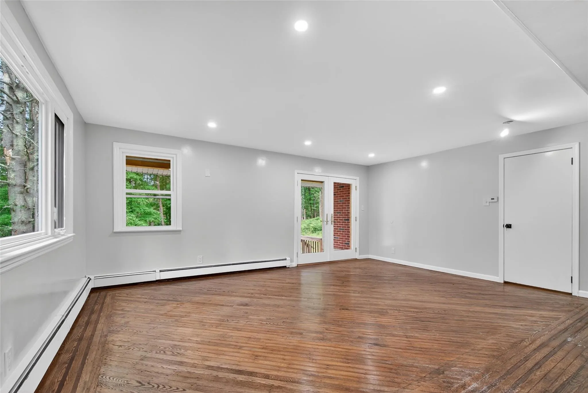 Unfurnished room with baseboard heating, wood finished floors, healthy amount of natural light, and recessed lighting Unfurnished room with baseboard heating, wood finished floors, healthy amount of natural light, and recessed lighting