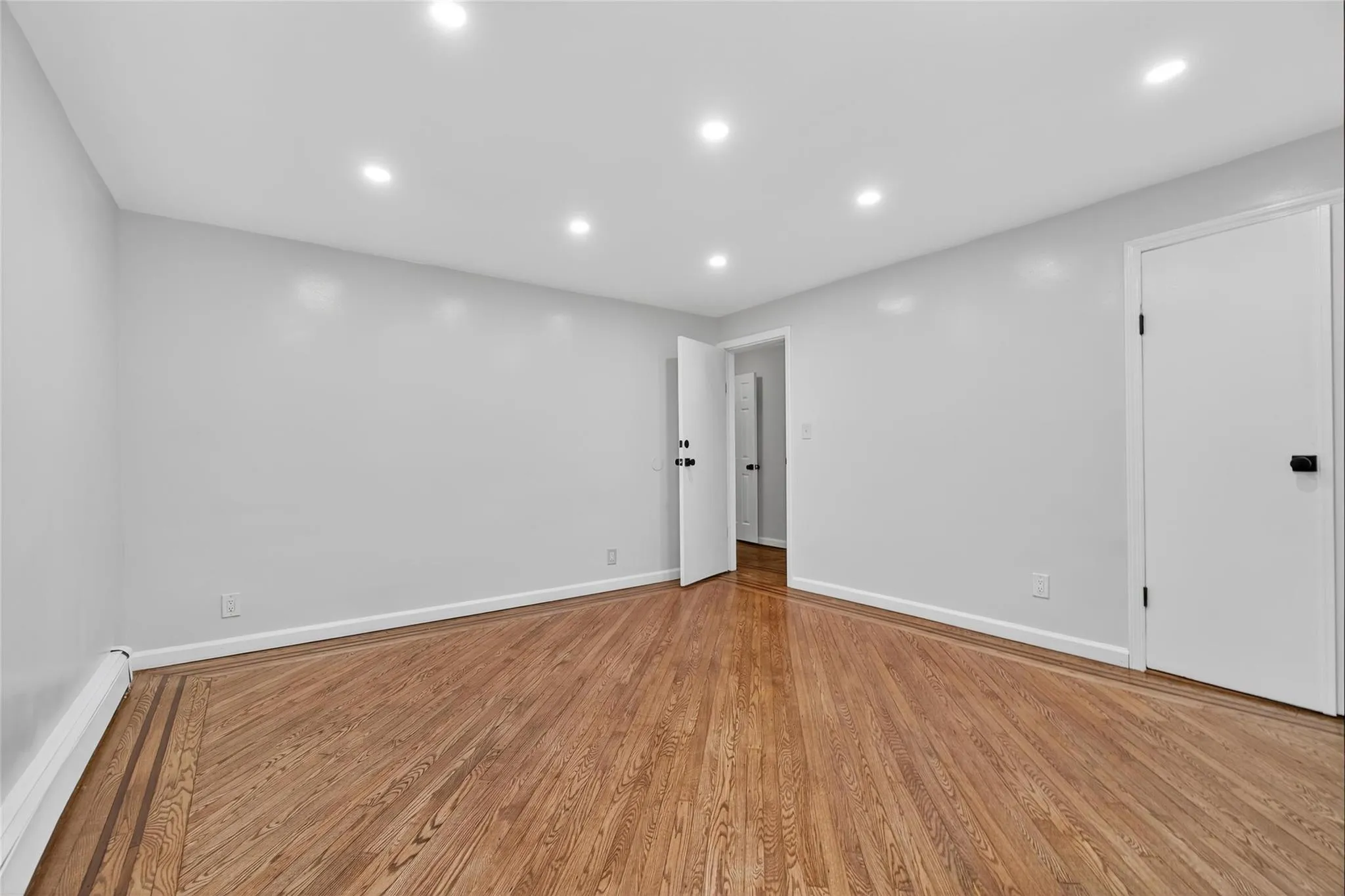 Empty room featuring light wood-type flooring, a baseboard heating unit, and recessed lighting Empty room featuring light wood-type flooring, a baseboard heating unit, and recessed lighting