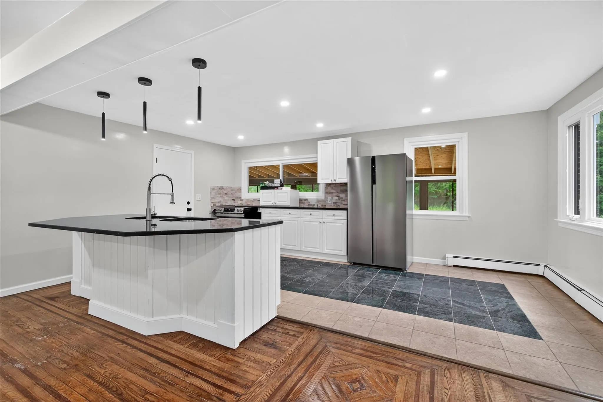 Kitchen featuring freestanding refrigerator, dark countertops, white cabinetry, decorative backsplash, and a kitchen island with sink Kitchen featuring freestanding refrigerator, dark countertops, white cabinetry, decorative backsplash, and a kitchen island with sink