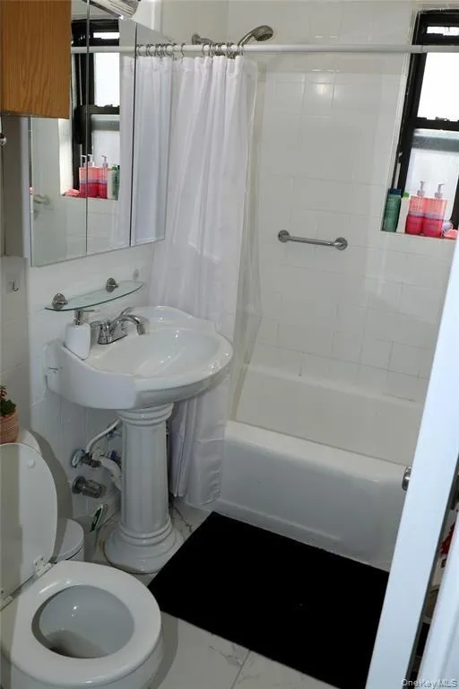 Bathroom featuring shower / bath combo with shower curtain and marble finish floors Bathroom featuring shower / bath combo with shower curtain and marble finish floors