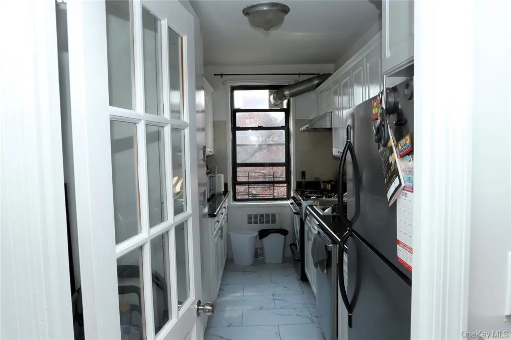 Kitchen with light marble finish floors, freestanding refrigerator, white cabinetry, white gas range oven, and range hood Kitchen with light marble finish floors, freestanding refrigerator, white cabinetry, white gas range oven, and range hood