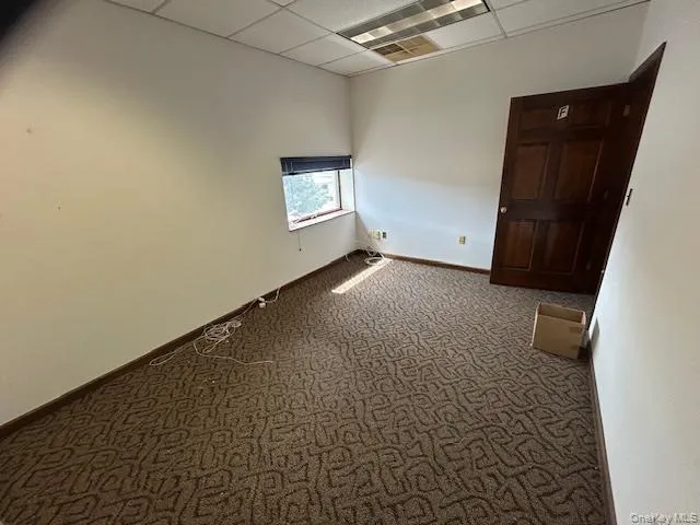 Carpeted empty room with a paneled ceiling and baseboards Carpeted empty room with a paneled ceiling and baseboards