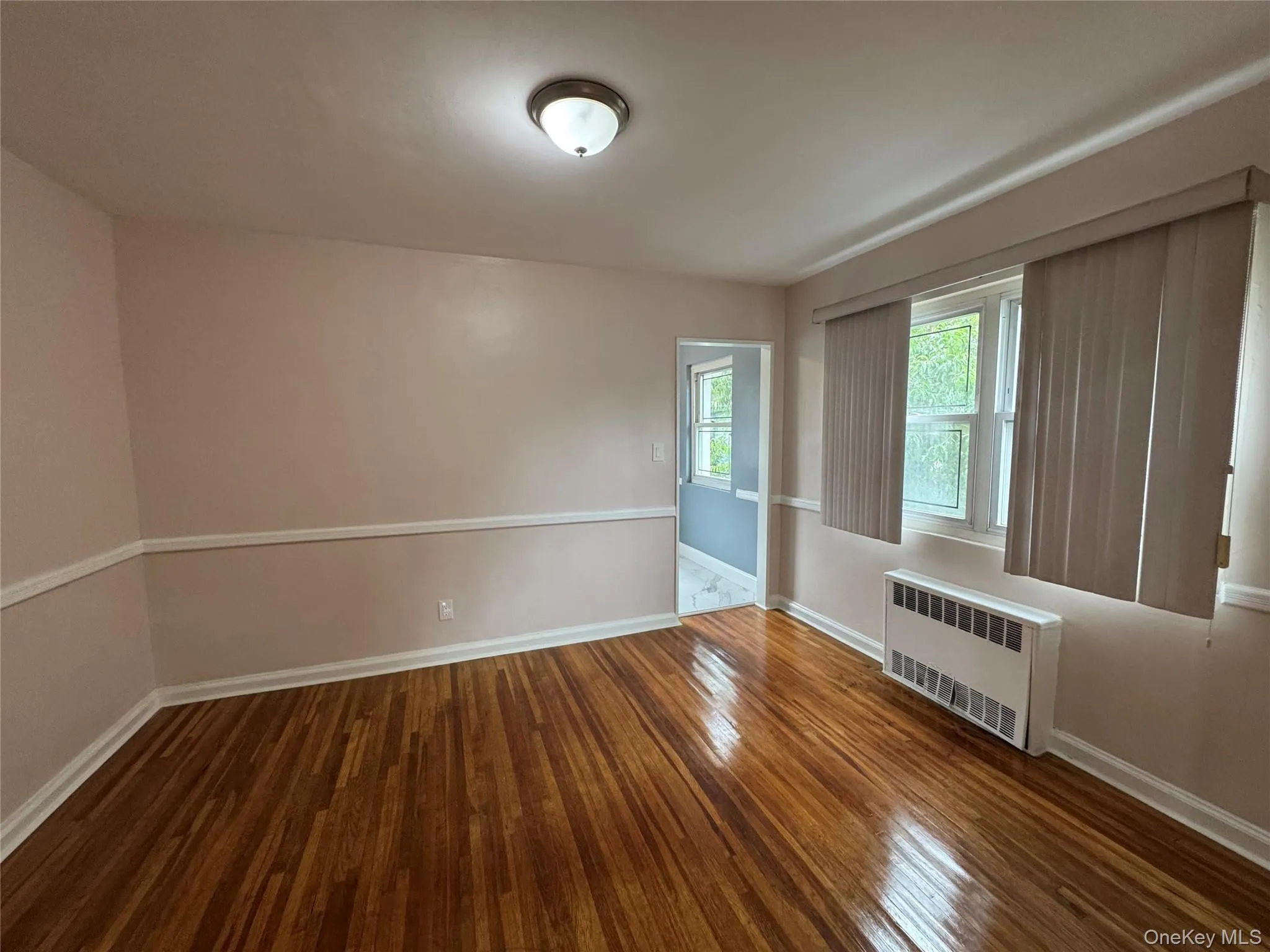 Unfurnished room with radiator heating unit and dark wood-style flooring Unfurnished room with radiator heating unit and dark wood-style flooring