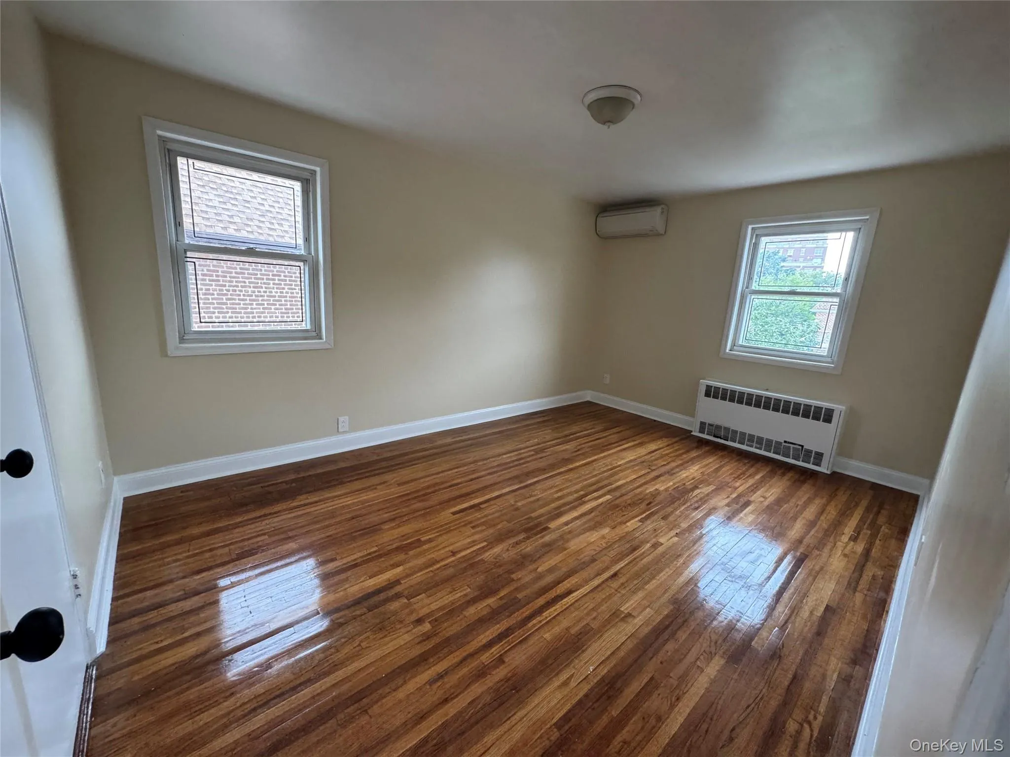 Empty room with hardwood / wood-style floors, radiator heating unit, and an AC wall unit Empty room with hardwood / wood-style floors, radiator heating unit, and an AC wall unit