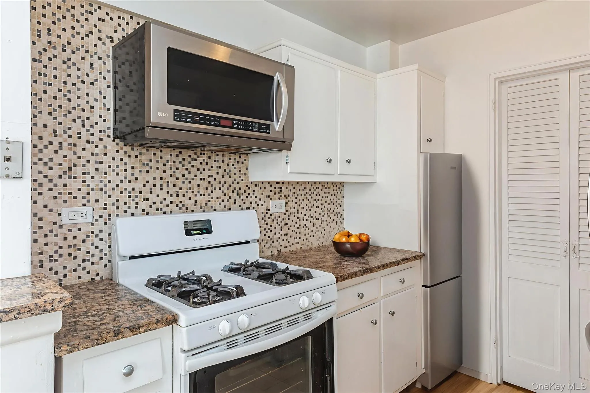 Kitchen with stainless steel appliances, decorative backsplash, white cabinets, and dark countertops Kitchen with stainless steel appliances, decorative backsplash, white cabinets, and dark countertops