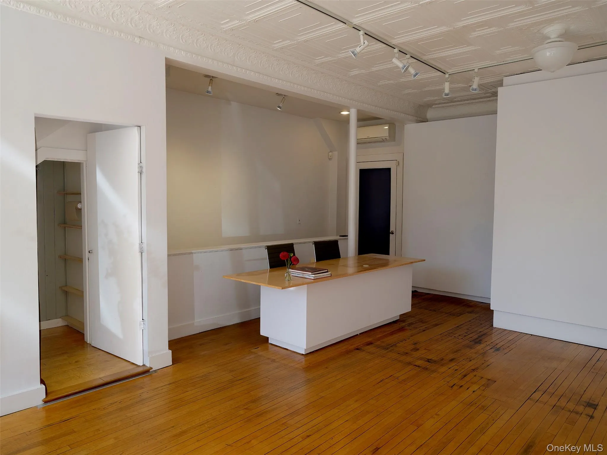 Kitchen featuring rail lighting, light wood-type flooring, a center island, white cabinets, and a wall mounted AC Kitchen featuring rail lighting, light wood-type flooring, a center island, white cabinets, and a wall mounted AC