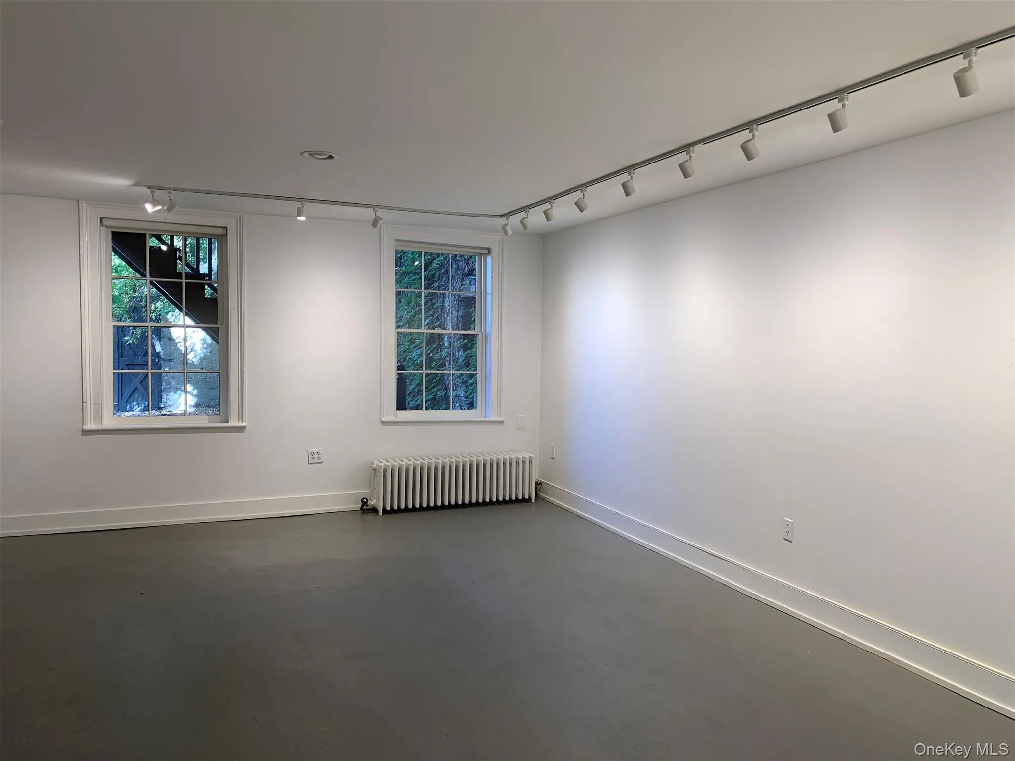 Spare room featuring rail lighting, radiator heating unit, and finished concrete floors Spare room featuring rail lighting, radiator heating unit, and finished concrete floors