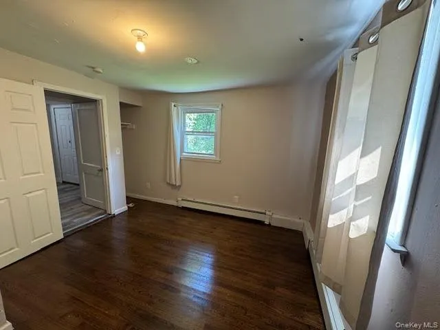 Unfurnished bedroom featuring wood finished floors and a baseboard heating unit Unfurnished bedroom featuring wood finished floors and a baseboard heating unit