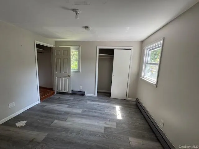 Unfurnished bedroom featuring a baseboard radiator, wood finished floors, and two closets Unfurnished bedroom featuring a baseboard radiator, wood finished floors, and two closets