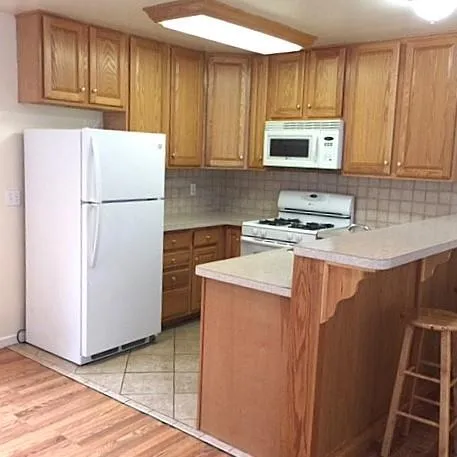 Kitchen featuring white appliances, a breakfast bar area, tasteful backsplash, light hardwood / wood-style flooring, and kitchen peninsula Kitchen featuring white appliances, a breakfast bar area, tasteful backsplash, light hardwood / wood-style flooring, and kitchen peninsula