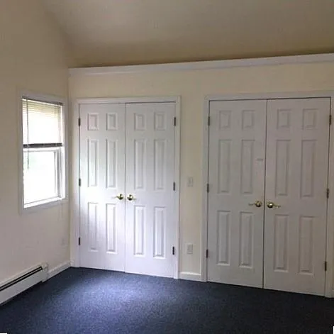 Unfurnished bedroom with lofted ceiling, multiple closets, a baseboard radiator, and dark colored carpet Unfurnished bedroom with lofted ceiling, multiple closets, a baseboard radiator, and dark colored carpet