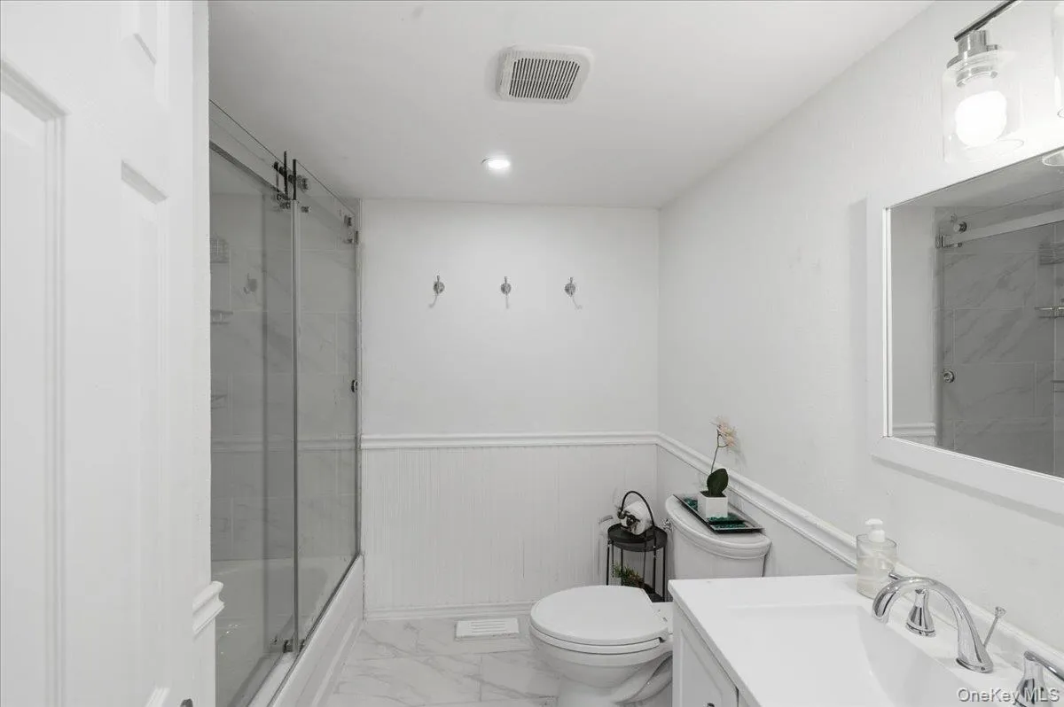 Bathroom featuring wainscoting, marble look tile flooring, vanity, combined bath / shower with glass door, and recessed lighting Bathroom featuring wainscoting, marble look tile flooring, vanity, combined bath / shower with glass door, and recessed lighting