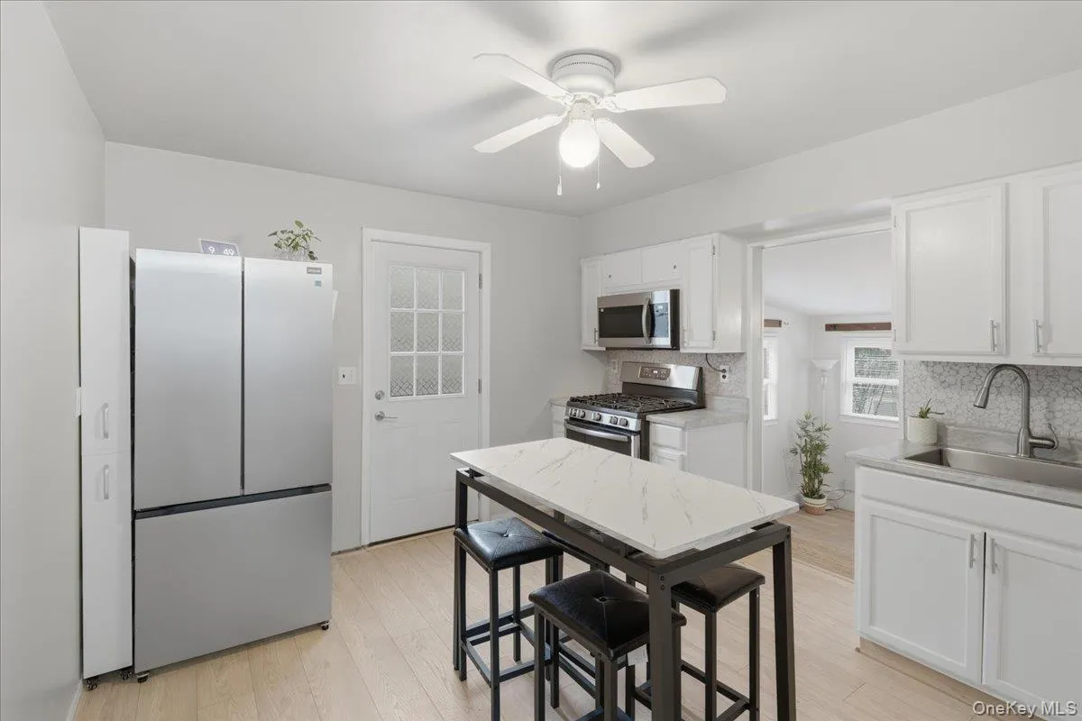 Kitchen featuring appliances with stainless steel finishes, white cabinets, decorative backsplash, light wood-style flooring, and a ceiling fan Kitchen featuring appliances with stainless steel finishes, white cabinets, decorative backsplash, light wood-style flooring, and a ceiling fan