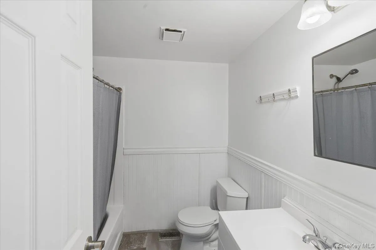 Full bathroom featuring a wainscoted wall, vanity, shower / bath combo with shower curtain, and a decorative wall Full bathroom featuring a wainscoted wall, vanity, shower / bath combo with shower curtain, and a decorative wall