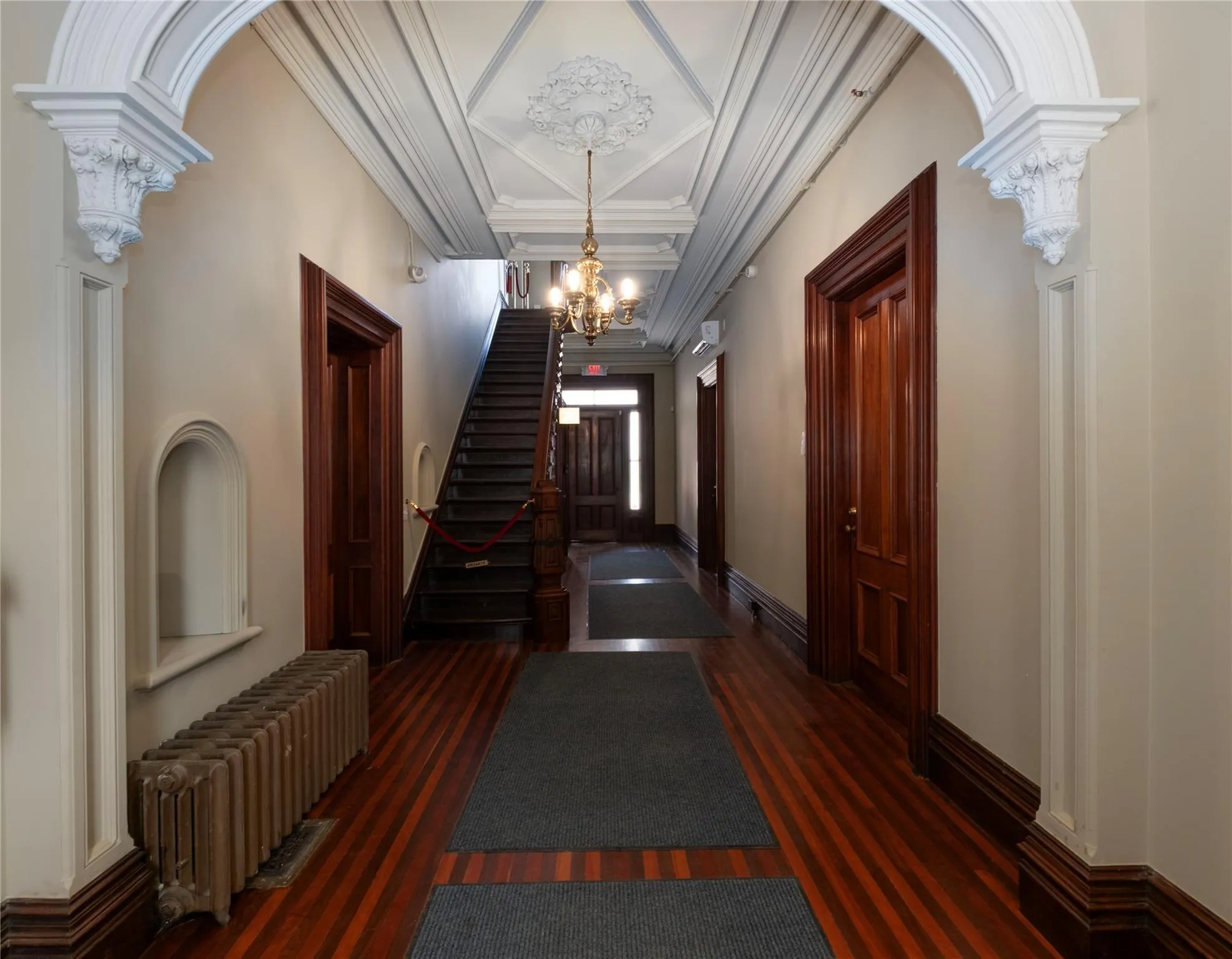 Hallway featuring radiator, a chandelier, wood finished floors, ornamental molding, and stairway Hallway featuring radiator, a chandelier, wood finished floors, ornamental molding, and stairway