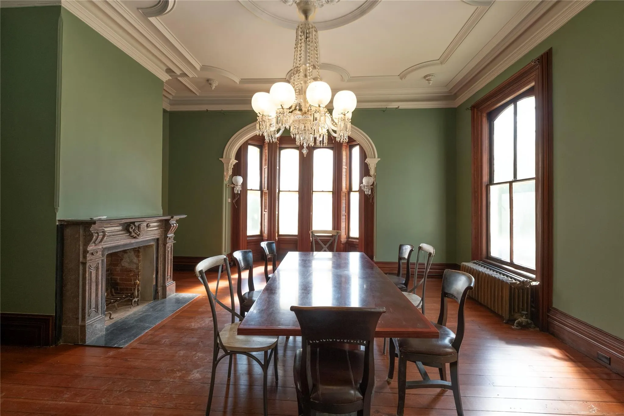 Dining room featuring a chandelier, radiator, wood-type flooring, a fireplace, and ornamental molding Dining room featuring a chandelier, radiator, wood-type flooring, a fireplace, and ornamental molding