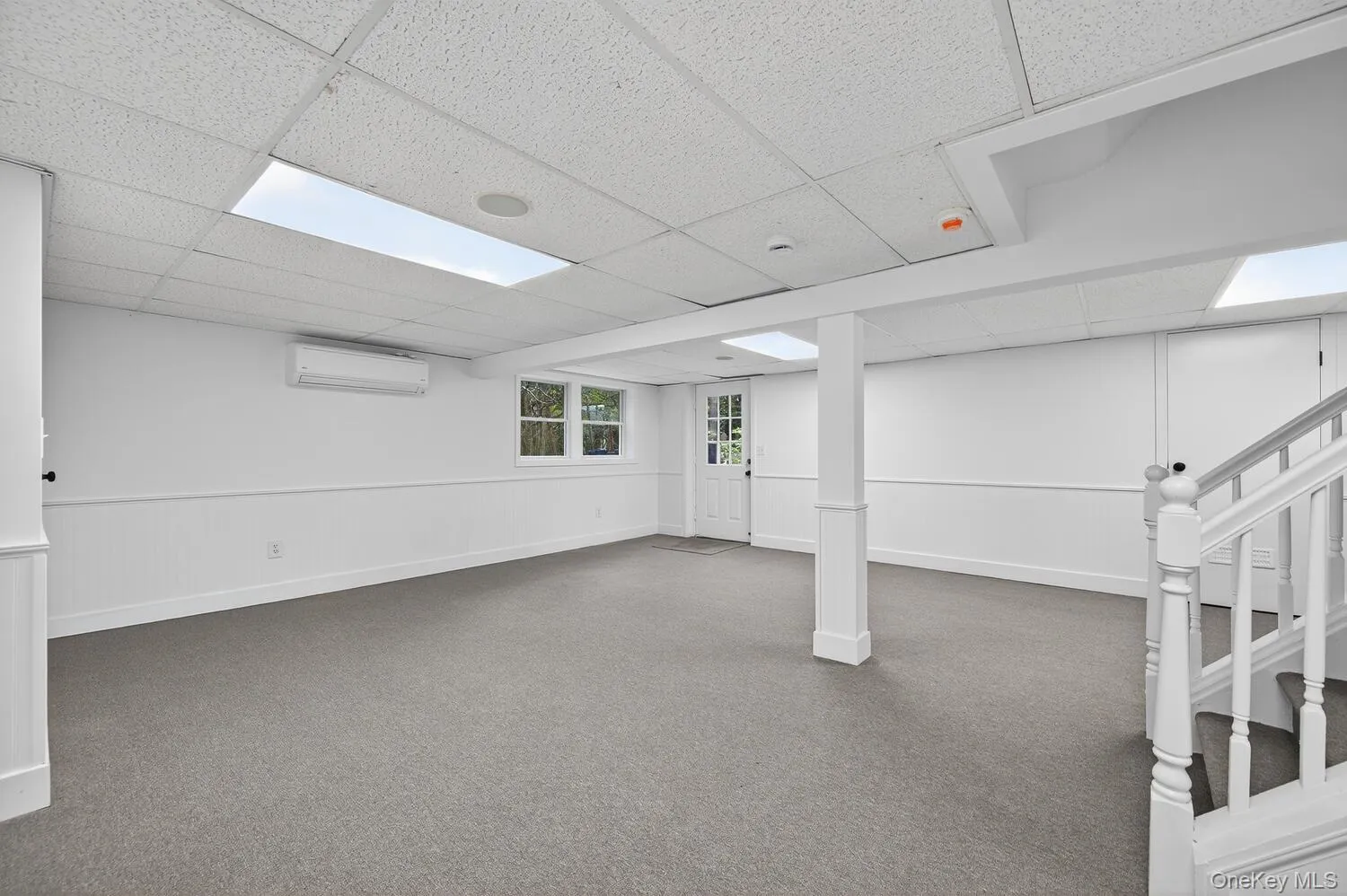 Basement with outside entrance with a paneled ceiling, carpet, a wall unit AC, and stairs Basement with outside entrance with a paneled ceiling, carpet, a wall unit AC, and stairs