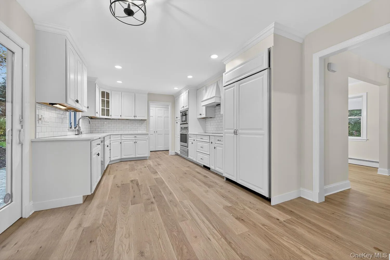 Kitchen with glass insert cabinets, backsplash, white cabinetry, light wood-type flooring, and a baseboard radiator Kitchen with glass insert cabinets, backsplash, white cabinetry, light wood-type flooring, and a baseboard radiator